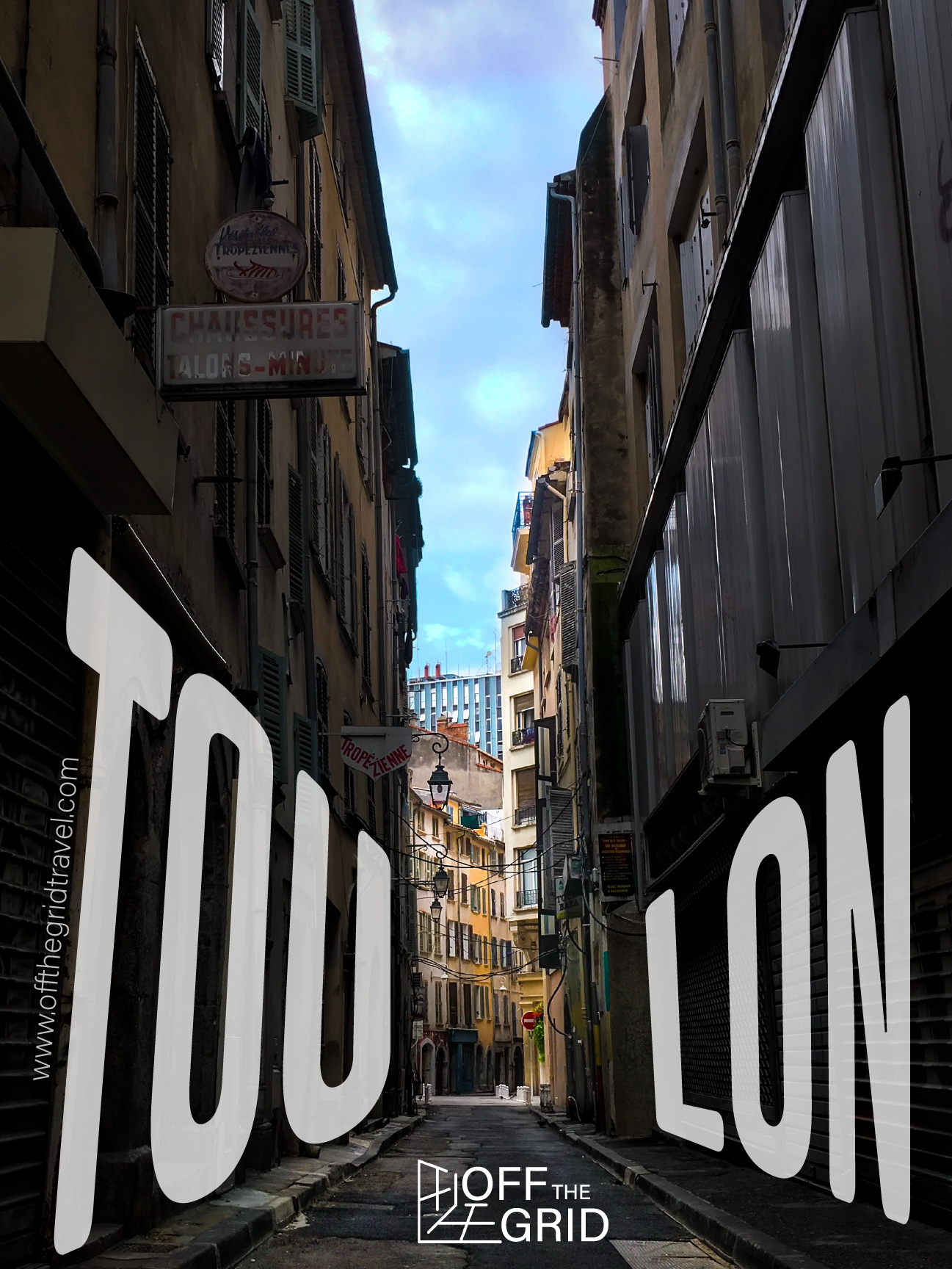 A narrow European city street with multi-story buildings on both sides; signs in French, including one that says "Chaussures Talons-Mince," and the sky visible at the end of the street.