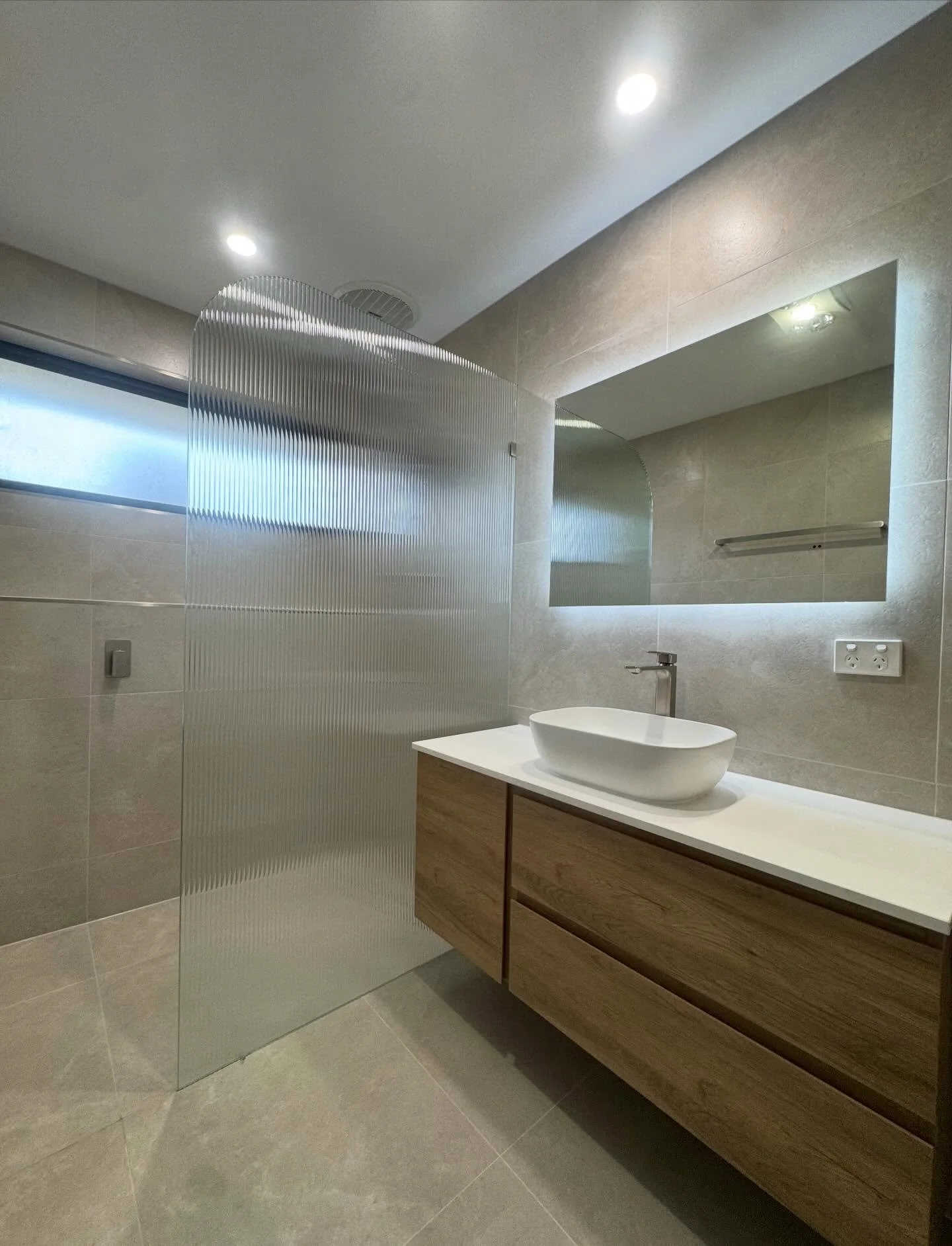 Noble Park bathroom renovation 

This renovation combines warm timber tones with soft neutral tiles to create a space that feels both inviting and refined. 
The floating vanity adds a sleek, contemporary touch, while the above-counter basin and brush