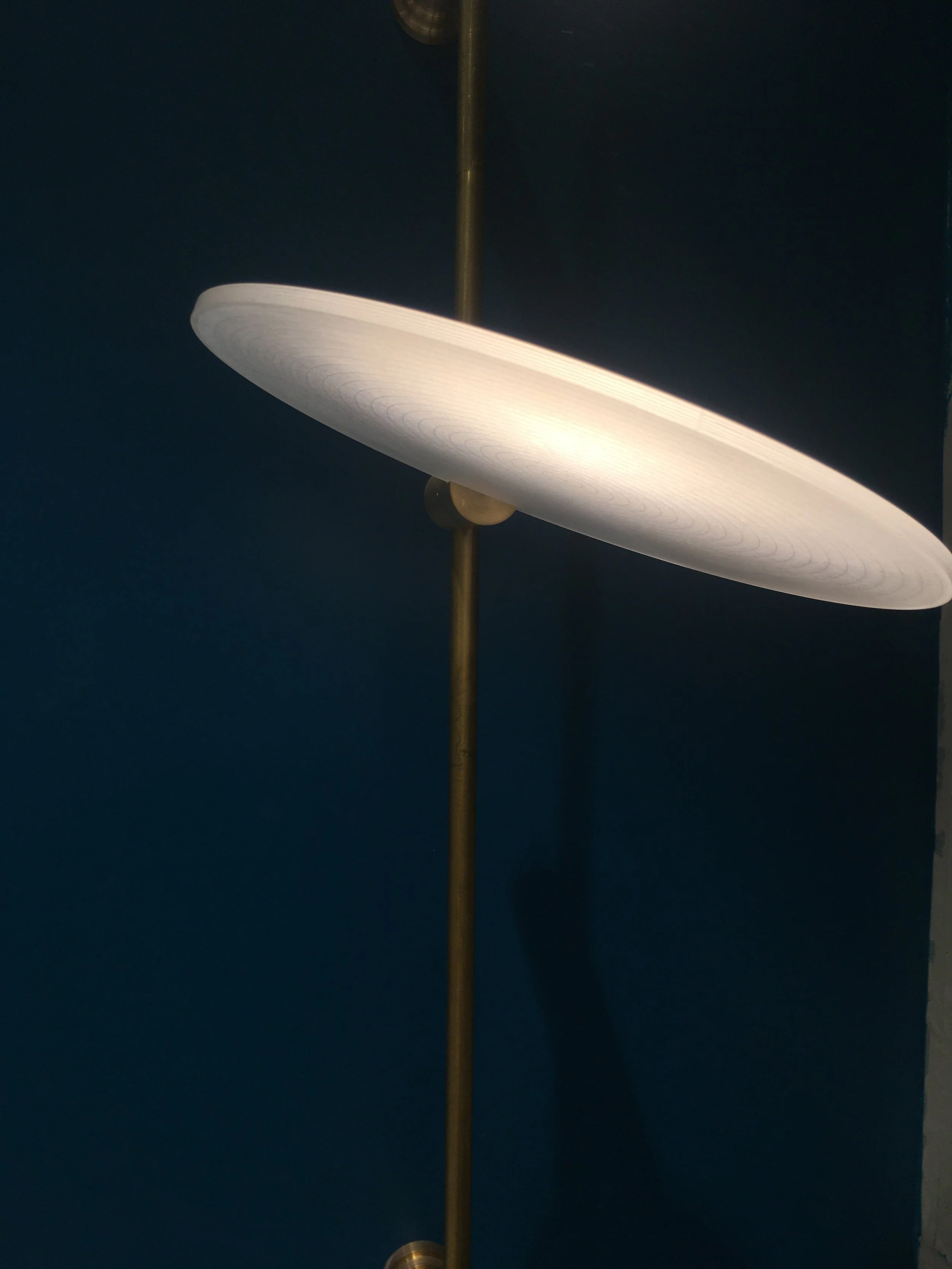 Modern brass floor lamp with a large round white lampshade against a dark blue wall.