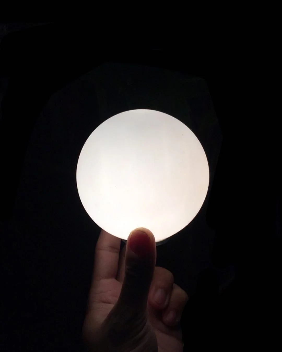 Hand holding a round, white object in darkness