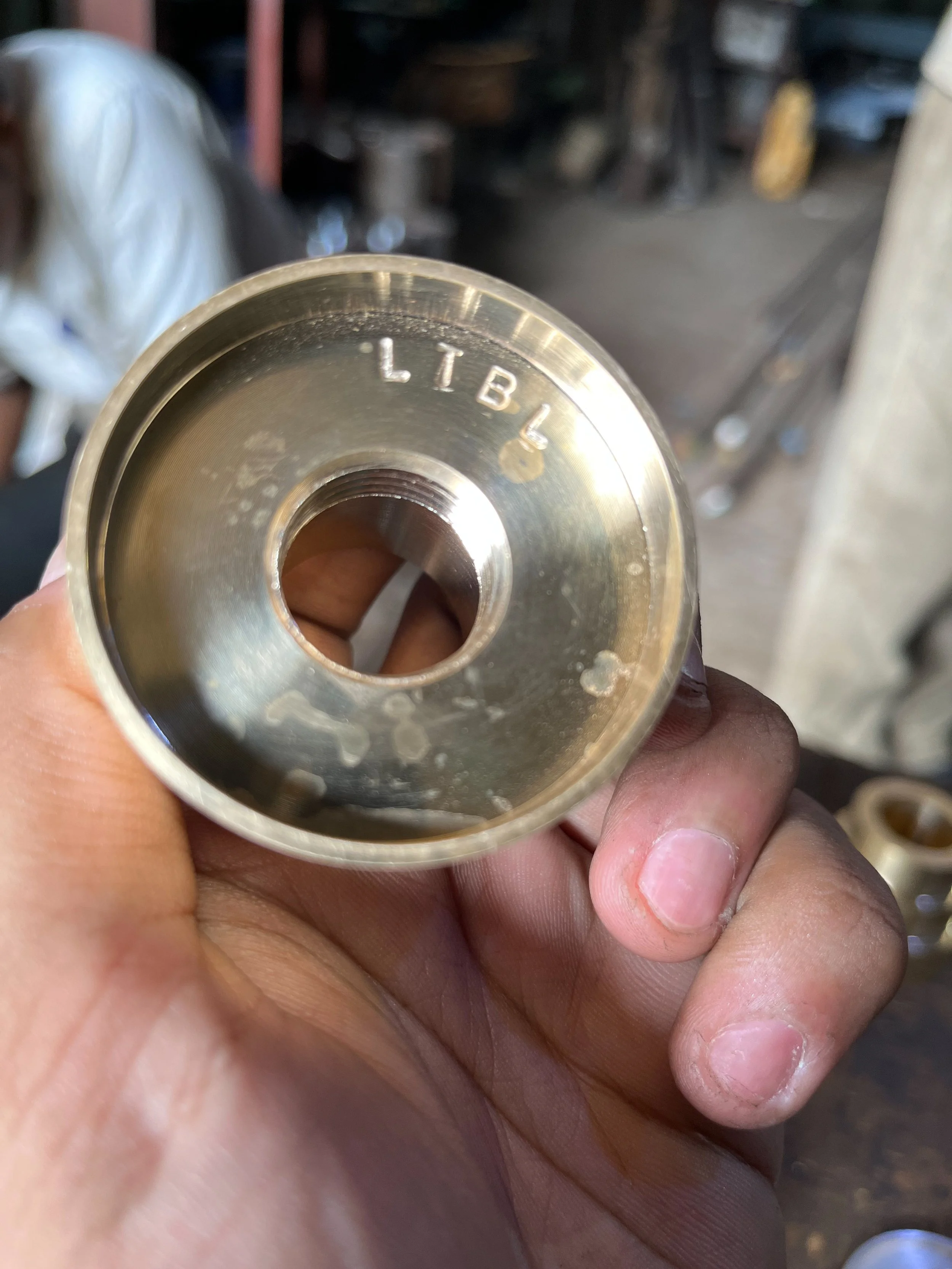 Close-up of a person's hand holding a metal part with "LTBL" engraved on it, possibly in a workshop setting.