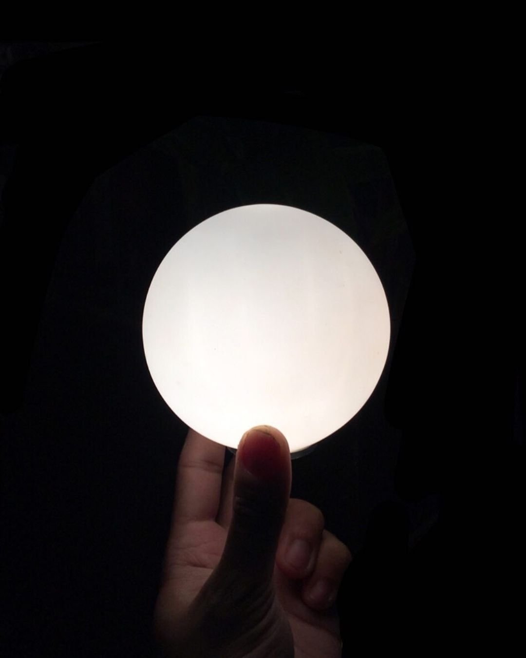 A hand holding a glowing circular object in a dark background.