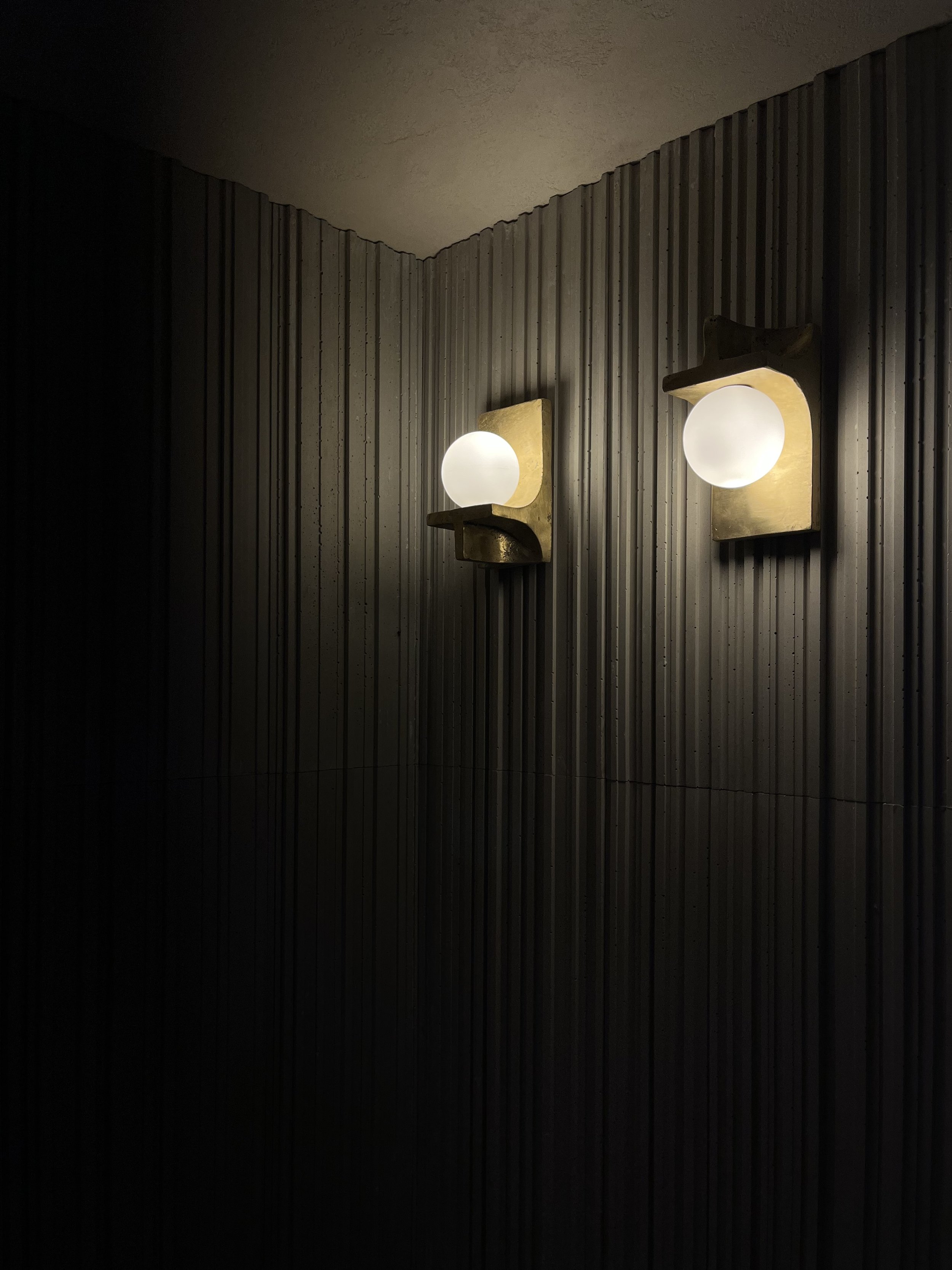 Two wall-mounted light fixtures with round frosted glass shades on a ribbed wall.