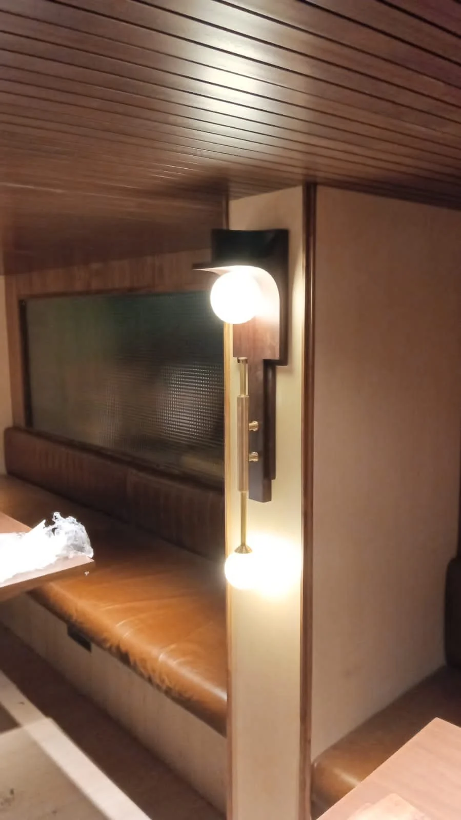 Cozy dining nook with brown leather bench seating, wooden ceiling, wall sconce, and glass partition.
