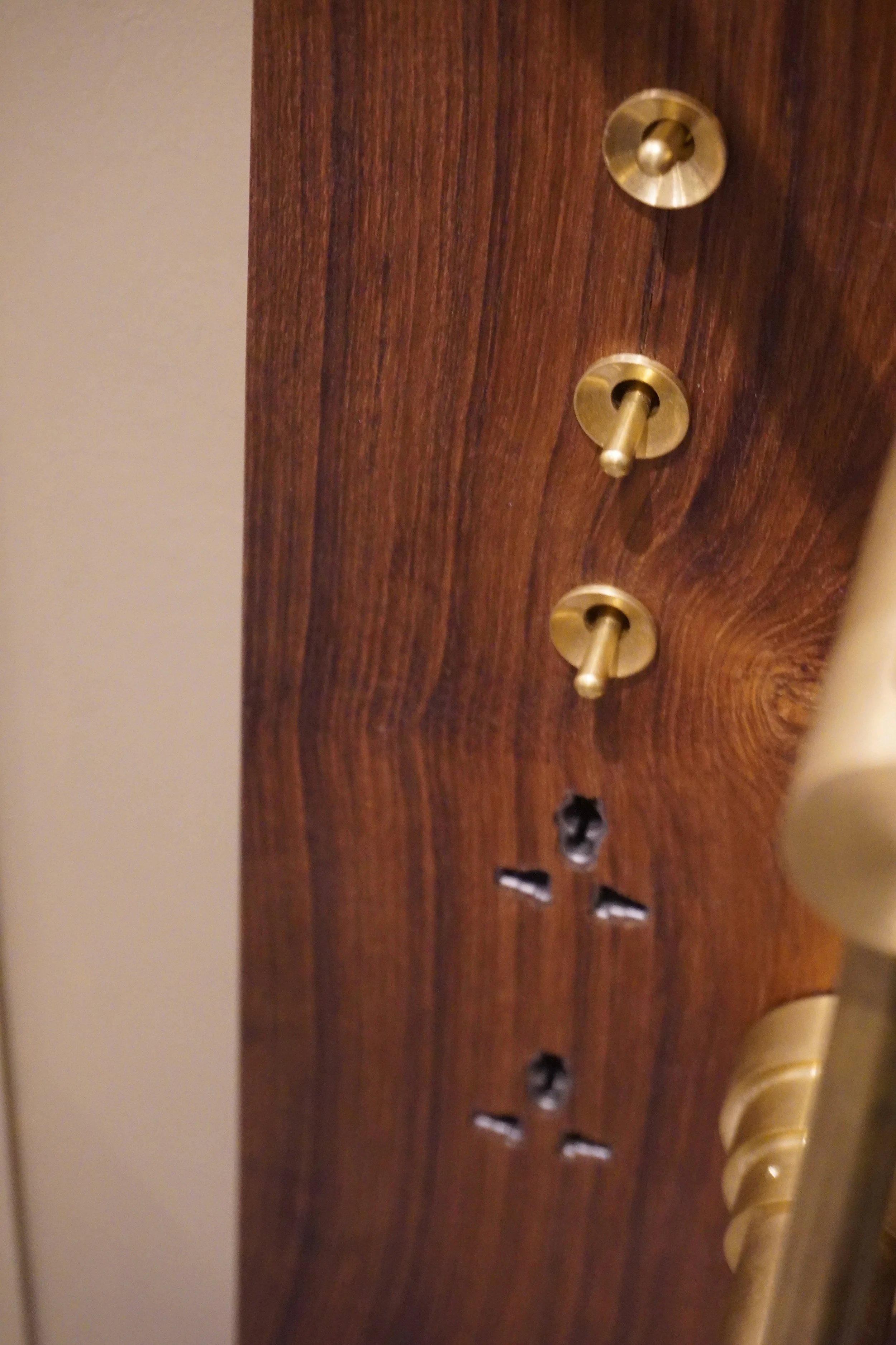 Close-up of a wooden panel with three brass toggle switches and three holes below them.