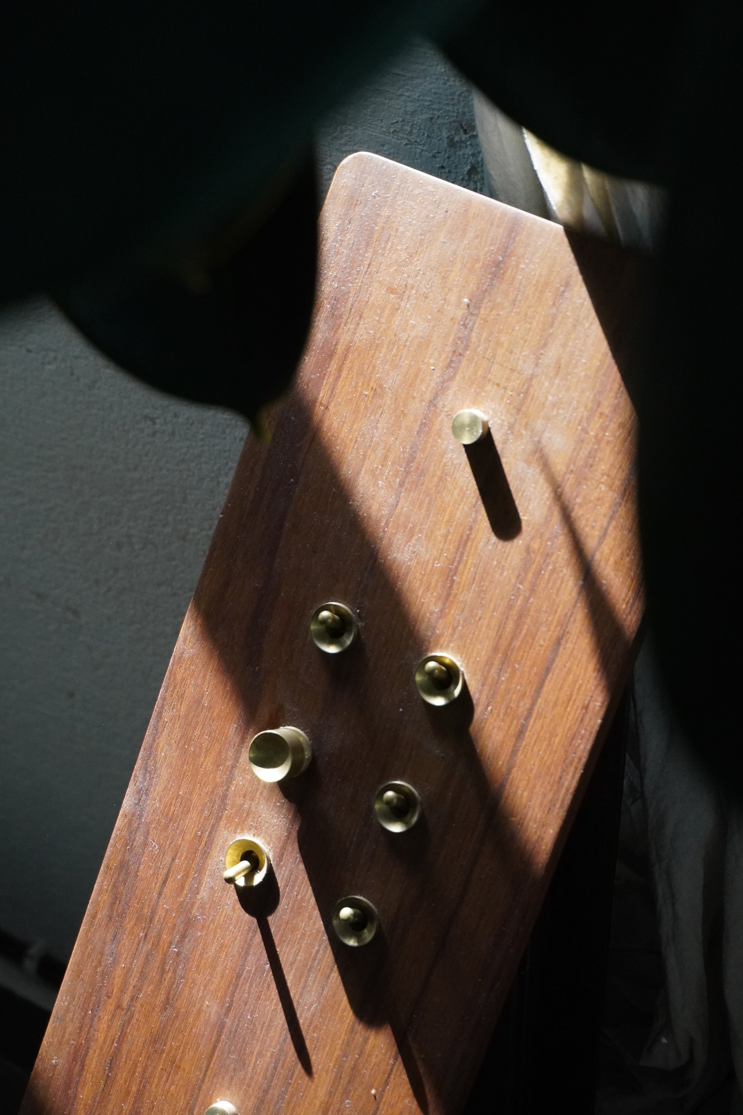 Close-up of a wooden board with metal pegs and knobs in sunlight.