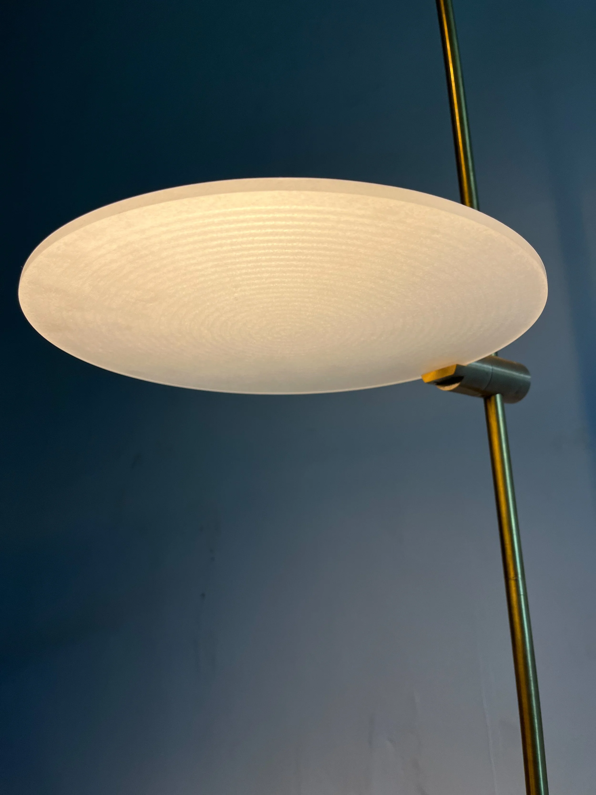 Modern floor lamp with a round, translucent lampshade on a tall, metal stand against a blue wall.