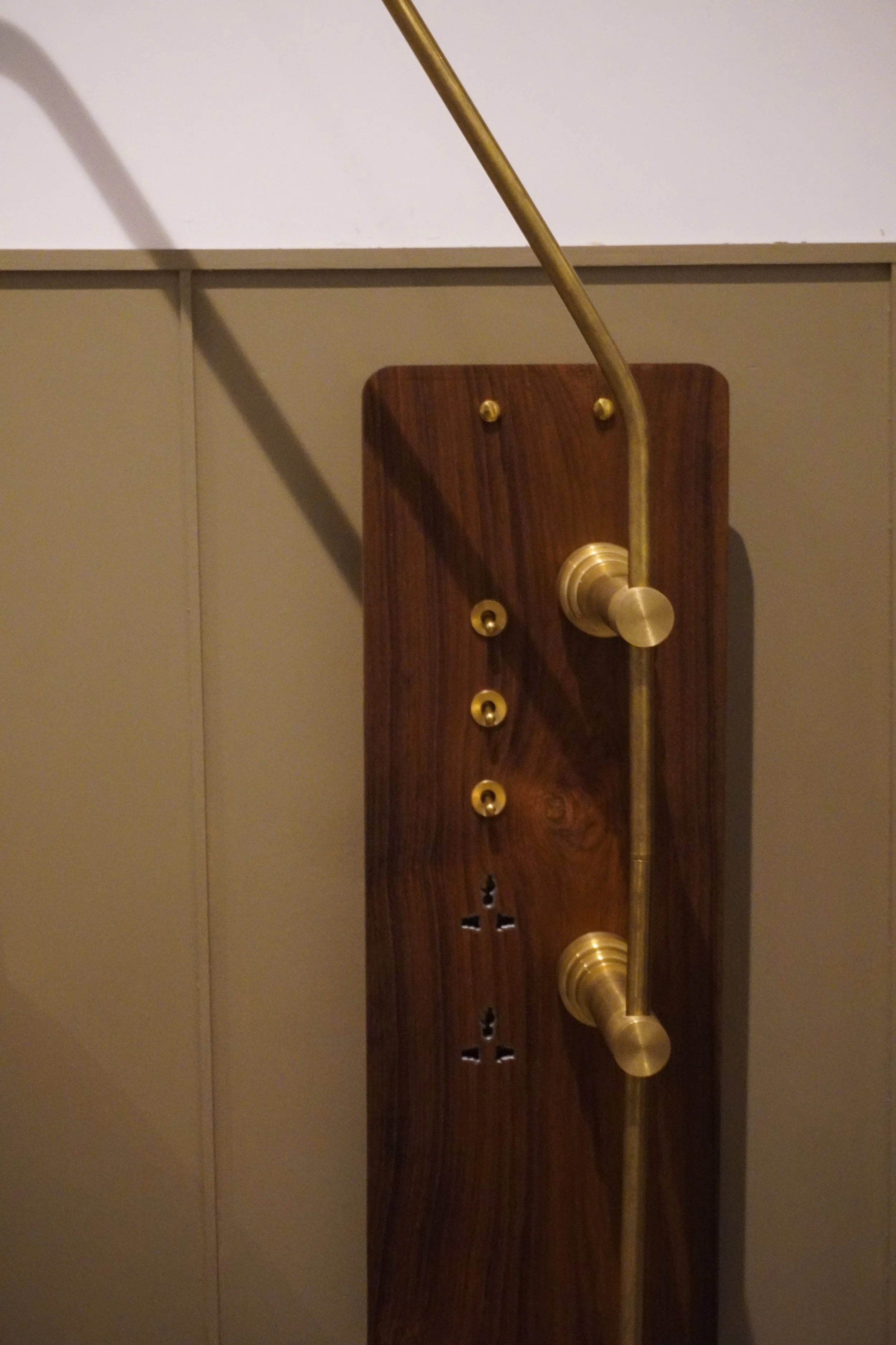 Wooden panel with brass coat hooks and a curved rod.