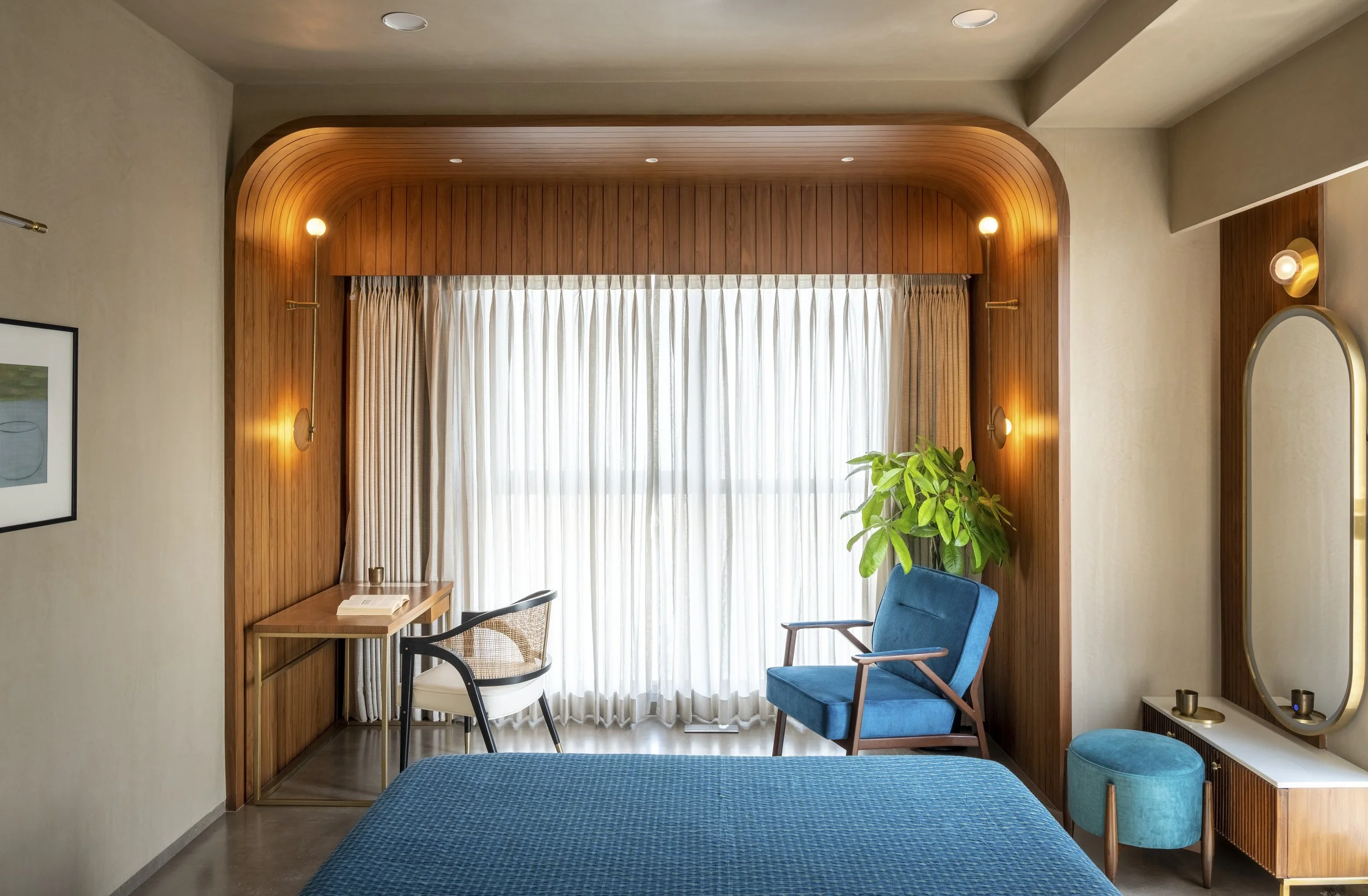 Modern bedroom with blue furniture, wooden decor, desk and chair near window, and potted plant