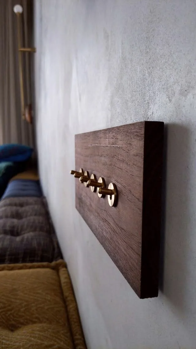 Wooden wall switch panel with brass toggle switches on a textured gray wall.
