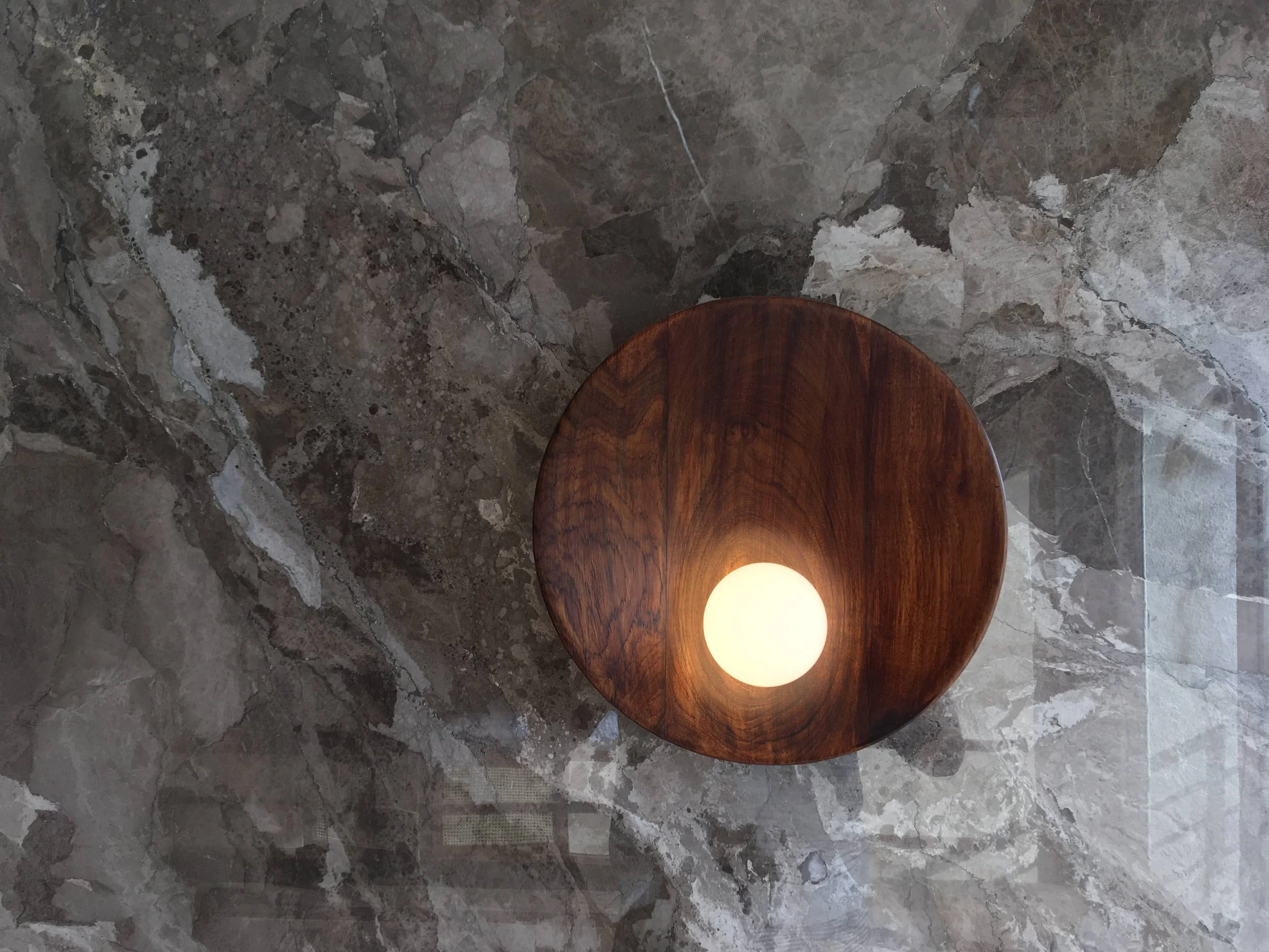 Top view of a round wooden light fixture with a glowing bulb on a textured stone surface.