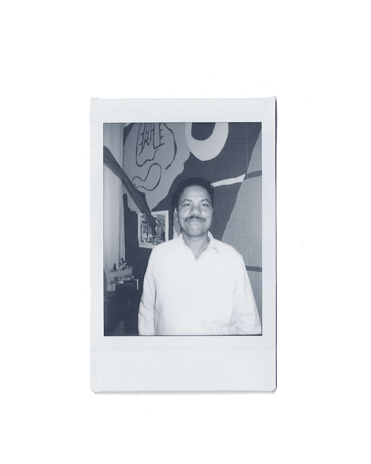 Black and white Polaroid of a man smiling in a room with abstract wall art. He is wearing a light-colored shirt.
