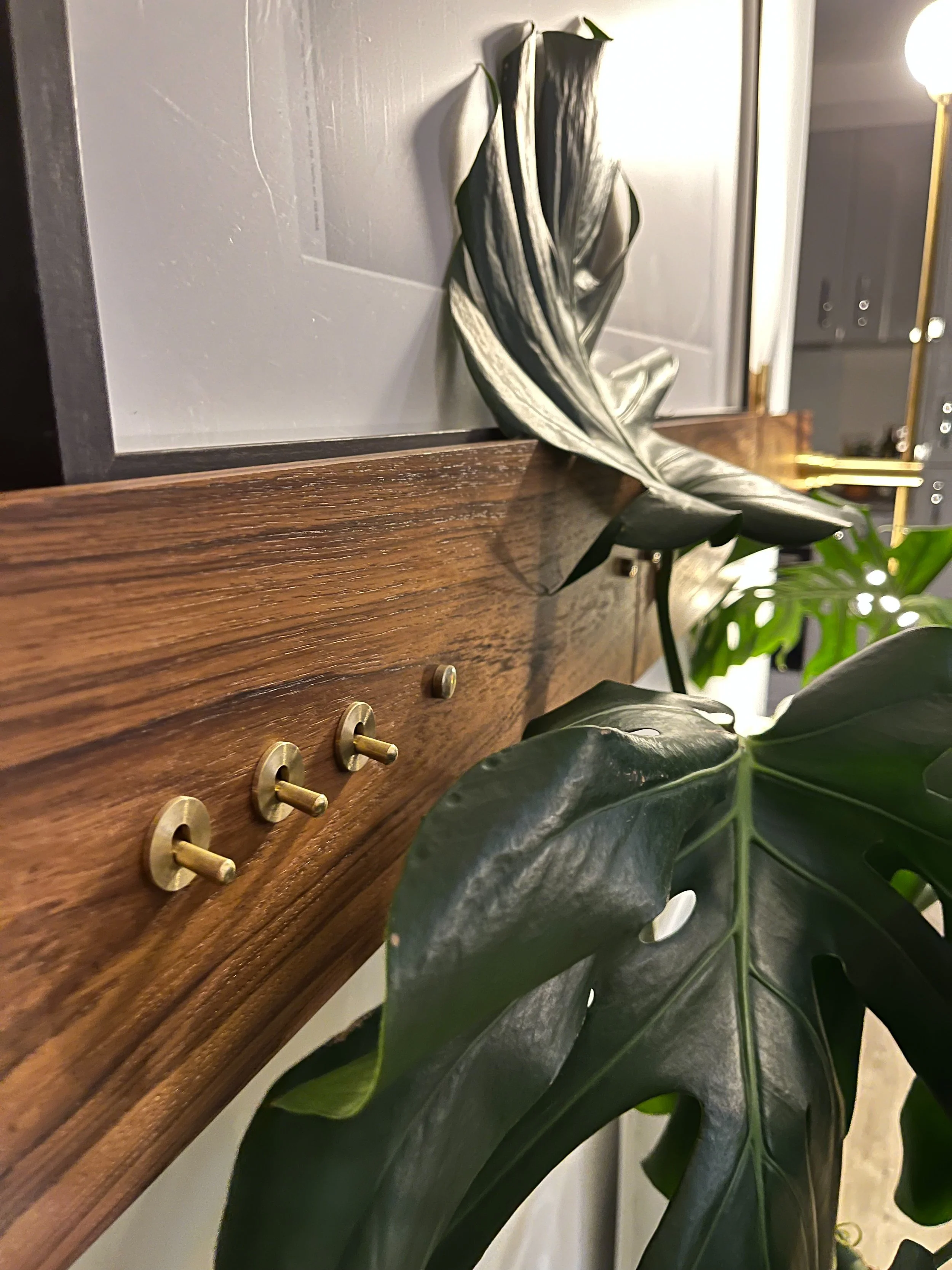 Close-up of a wooden surface with brass switches, partial view of tropical leaves, and a soft-focus background with warm lighting.