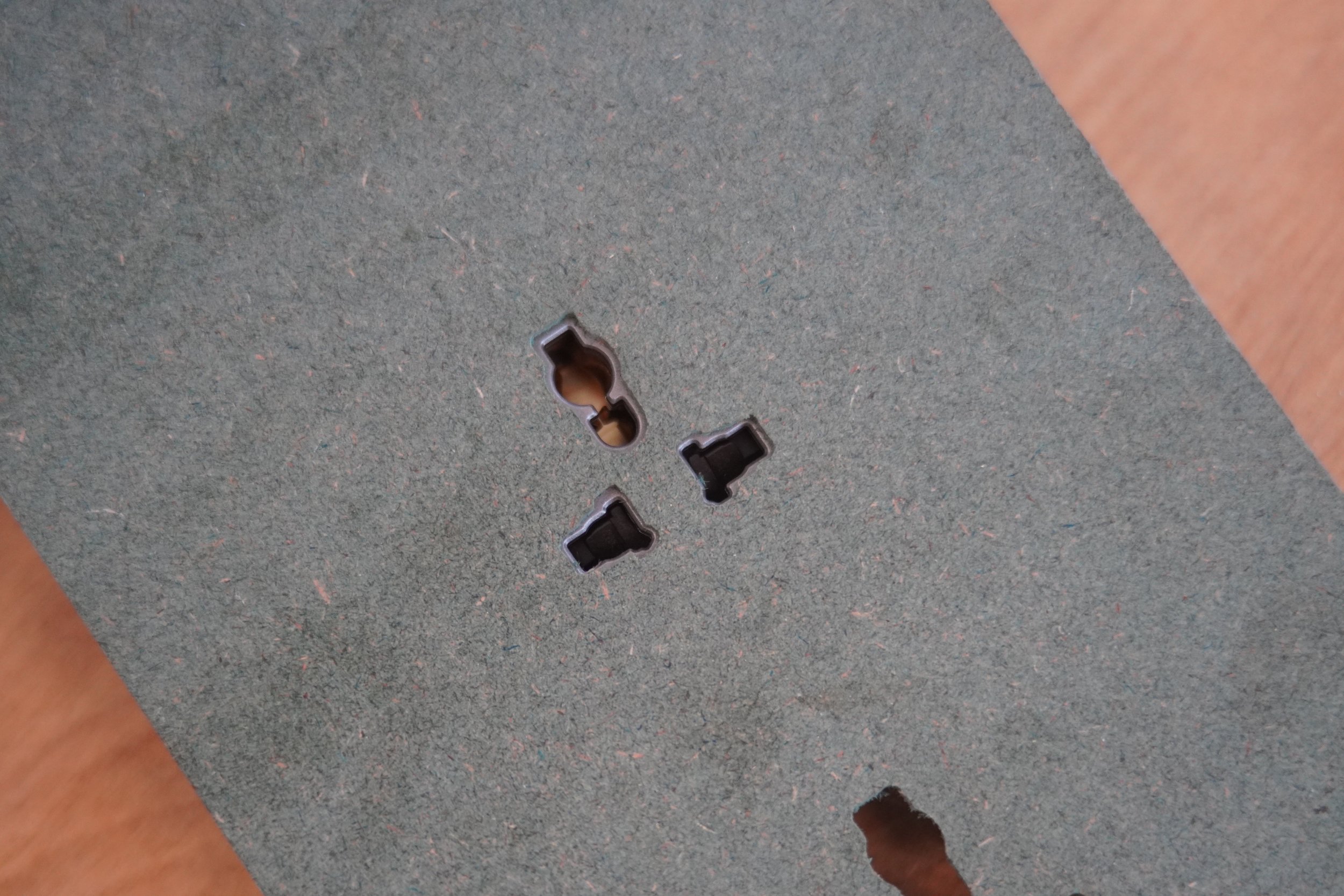 Gray fiberboard with drilled holes and a wooden texture in the background.