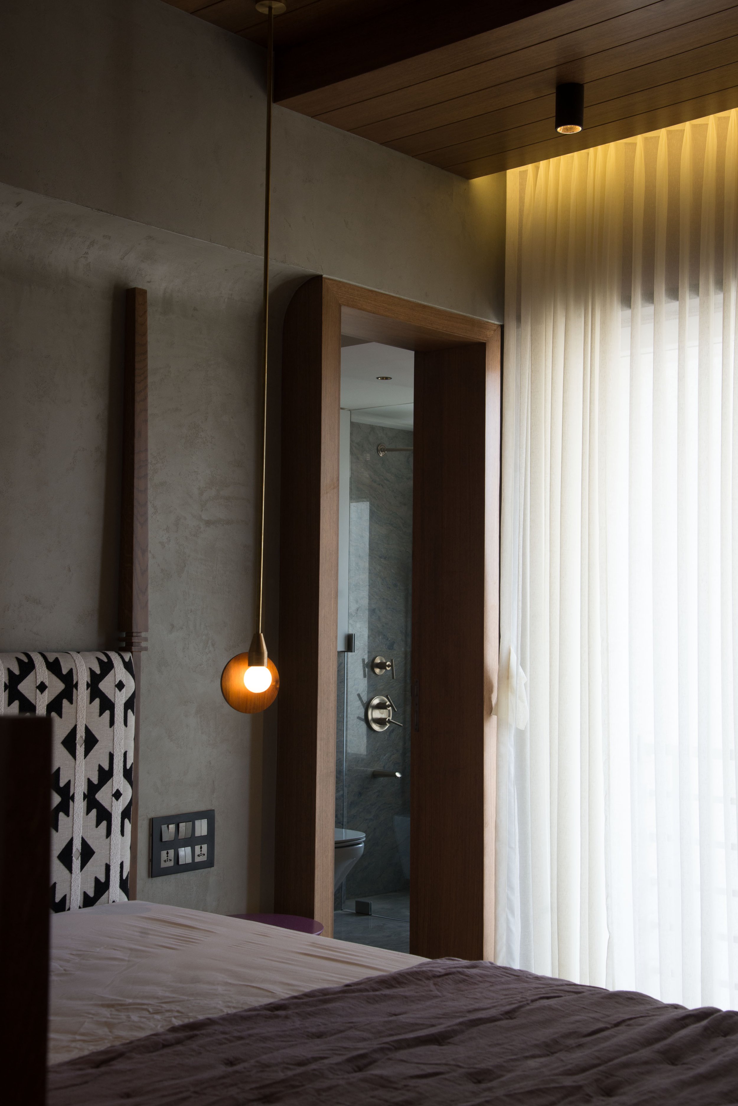 Modern bedroom interior with a pendant light, patterned headboard, and doorway leading to a bathroom.