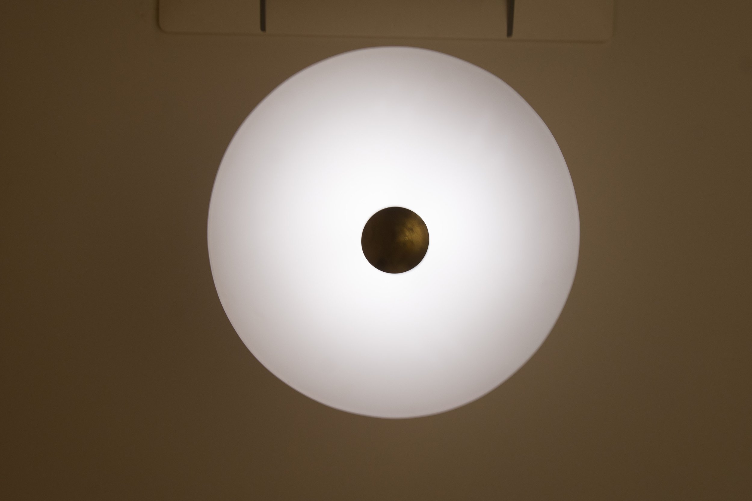 Ceiling light with circular design and central dark spot on a beige background.