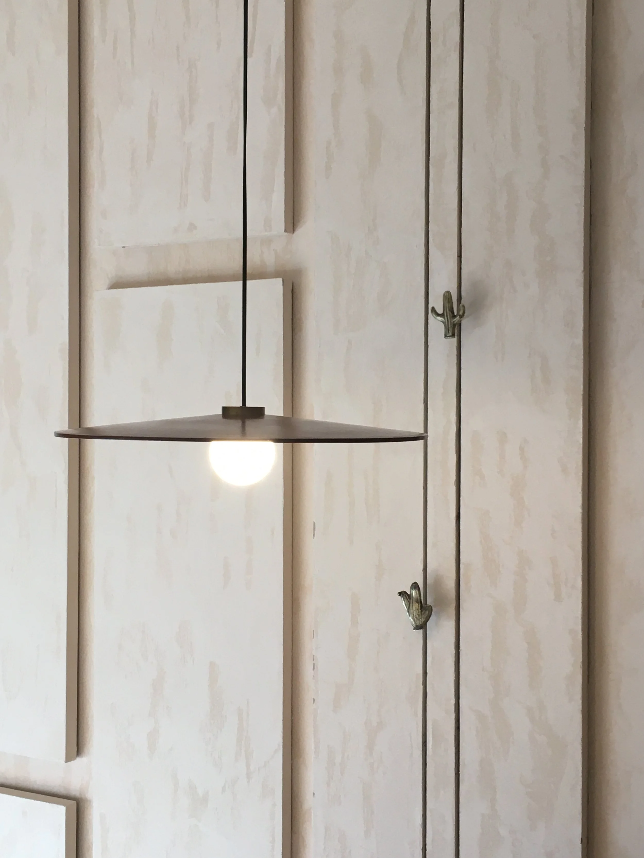 Minimalist pendant light against a textured beige wall with decorative panels and metal cactus hooks.