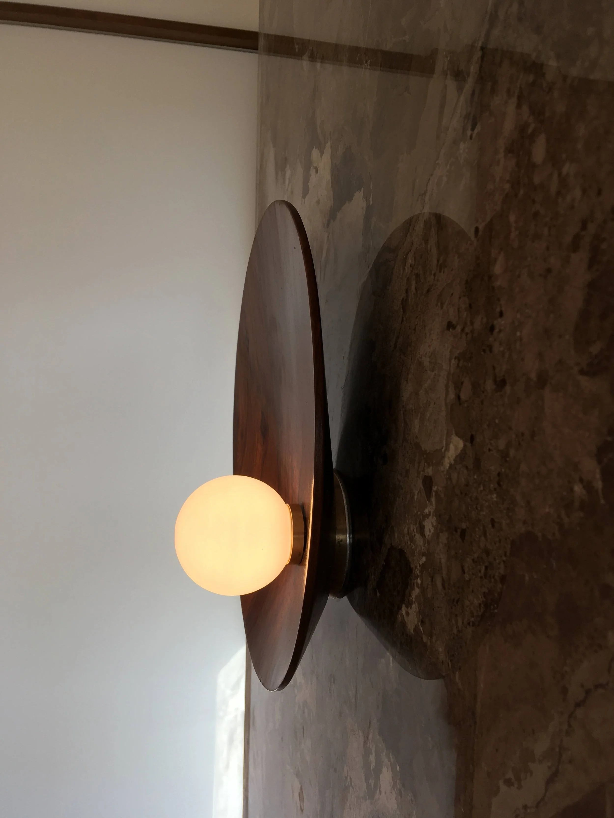 A round, modern table lamp with a wooden base and a frosted glass globe shade, set on a stone surface.