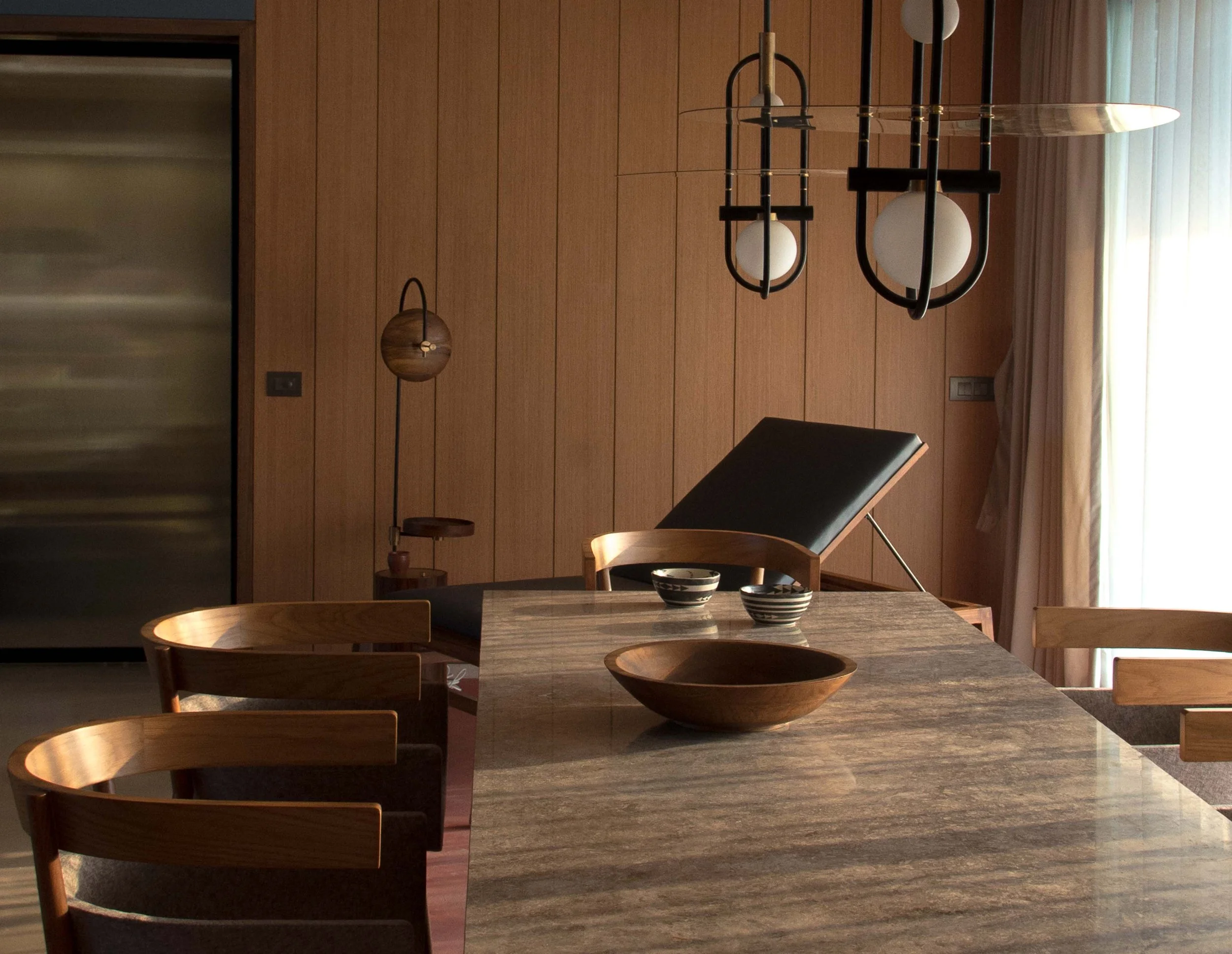 Modern dining room with wooden chairs, a marble table, a wooden bowl, ombre vertical blinds, and contemporary pendant lighting.