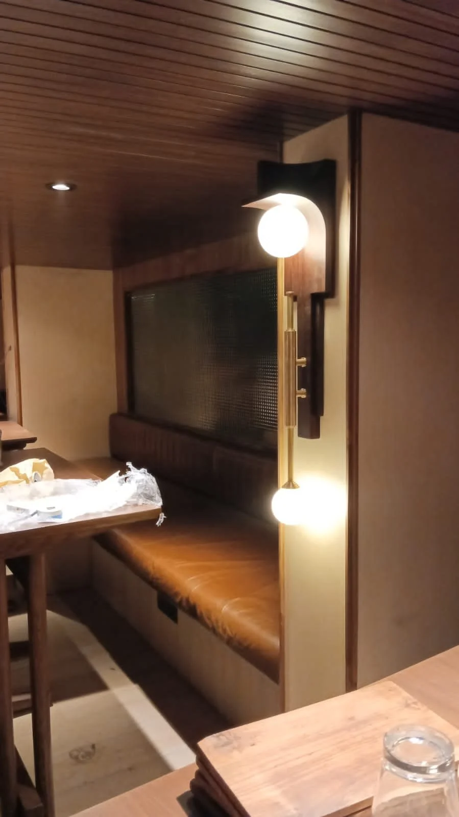 Wooden dining area with leather bench seating, overhead lighting, wooden walls, and a glass partition.