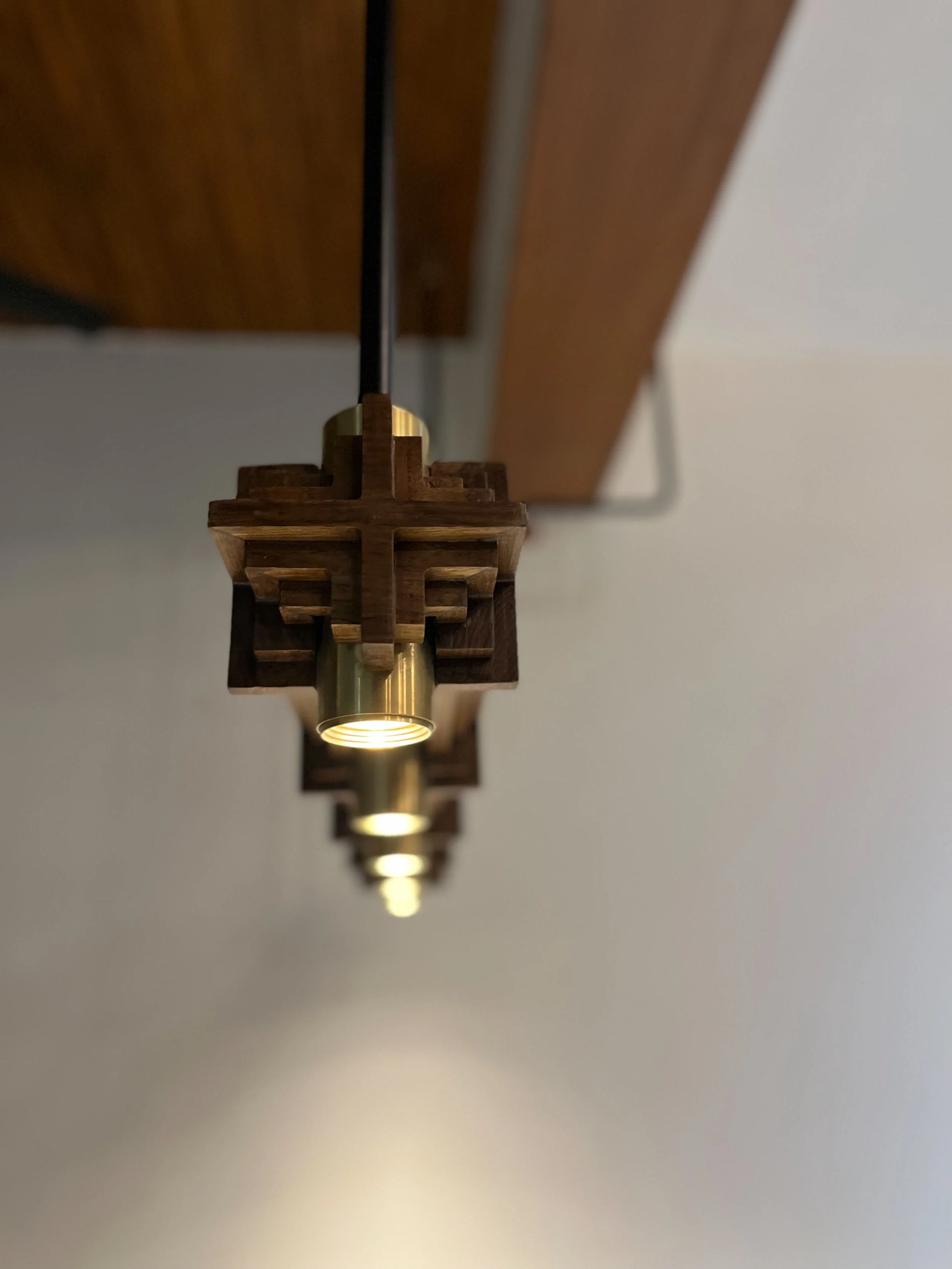 Close-up of a series of hanging light fixtures with wooden and metallic elements, mounted in a linear arrangement on the ceiling.