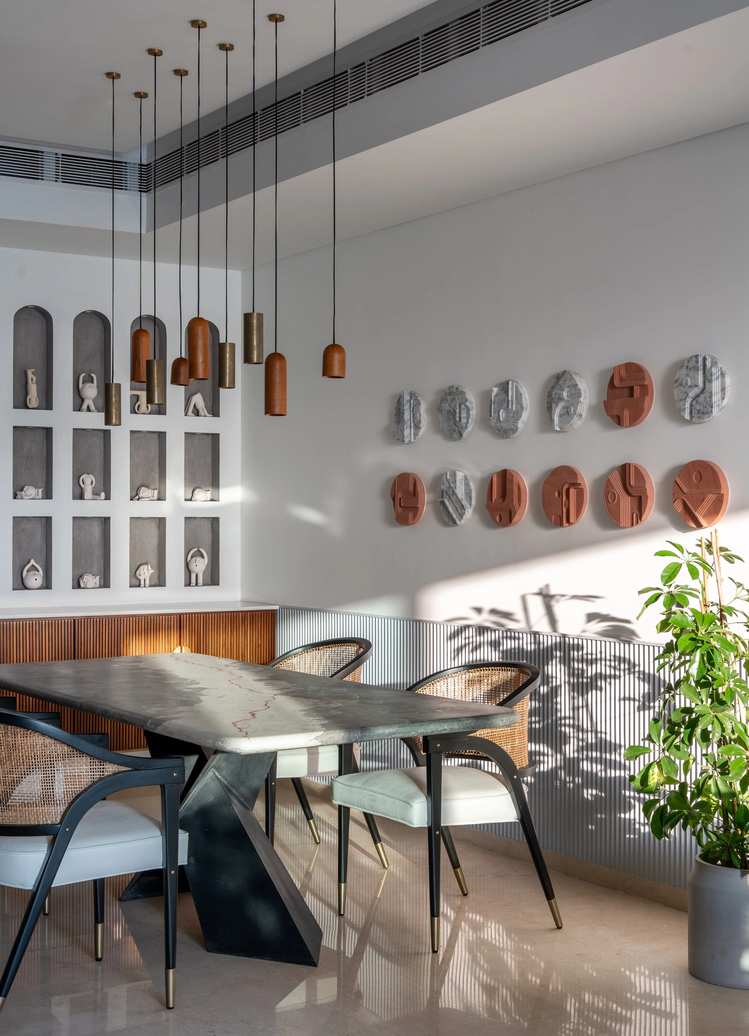 Modern dining room with a sleek table, stylish chairs, and pendant lights. Decorative wall art features abstract designs, and a plant adds greenery.