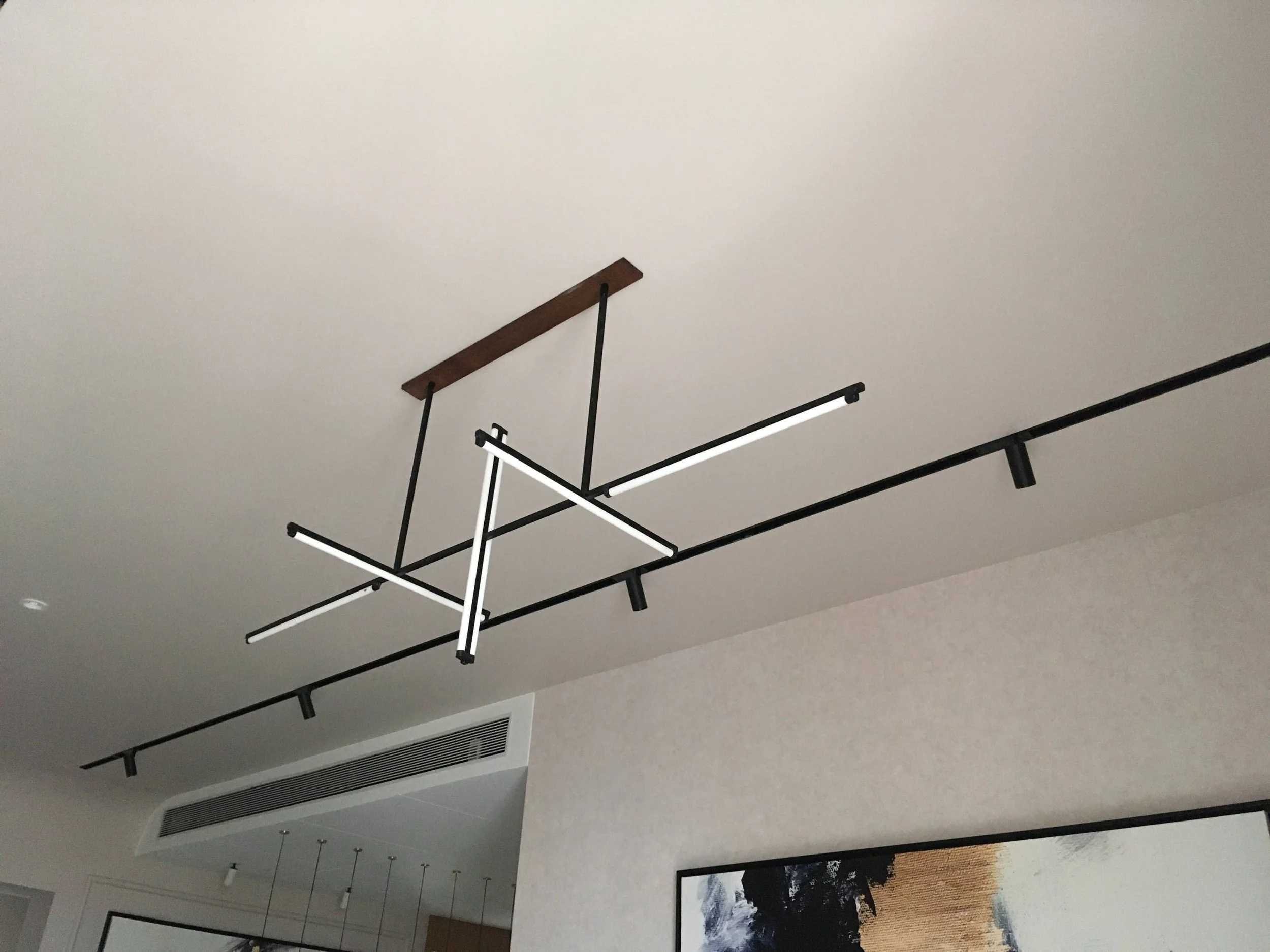 Modern black metal ceiling light fixture with intersecting rods and LED lights in a minimalist room setting.