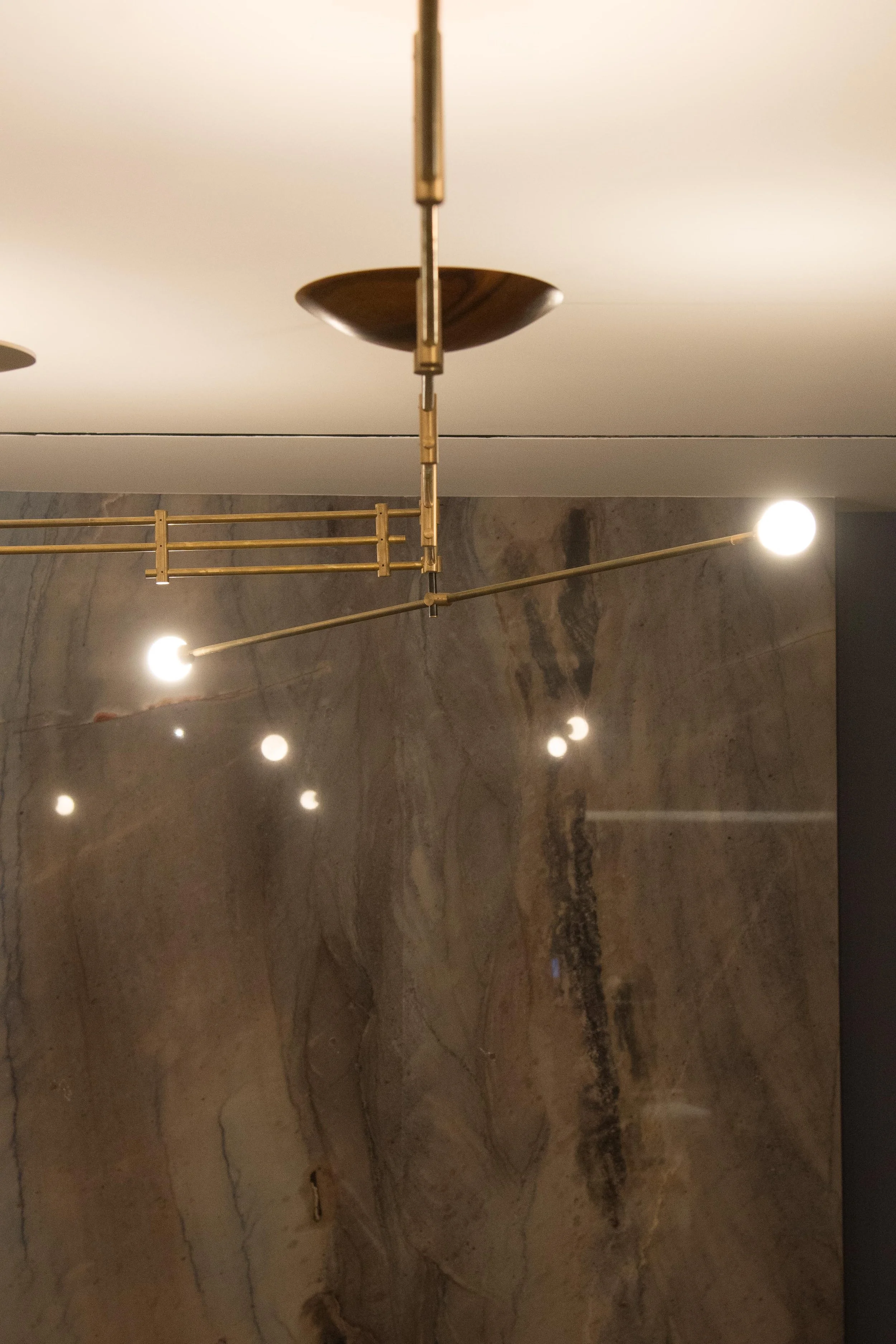 Modern ceiling light fixture with glowing bulb, set against a marble wall.