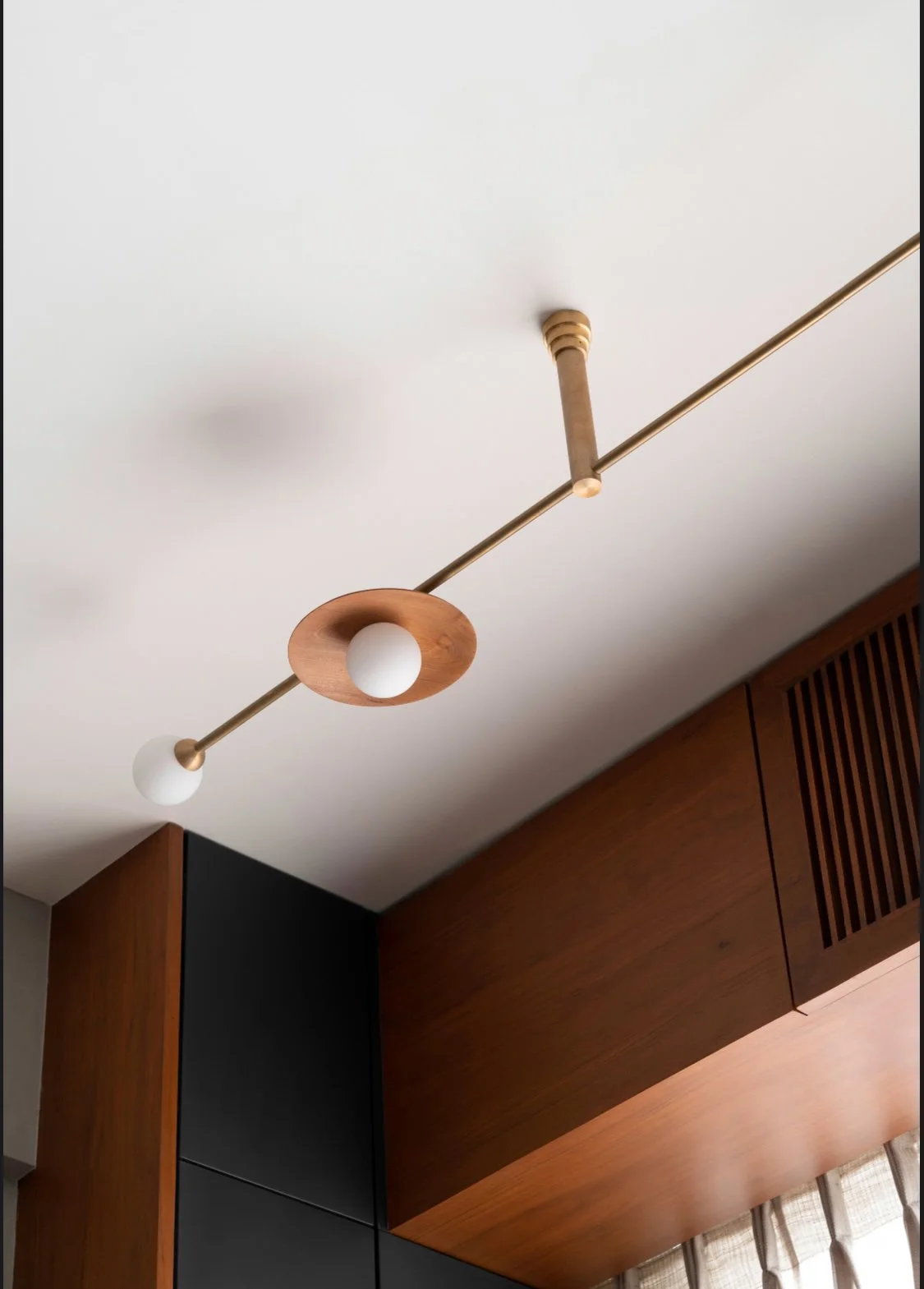 Modern ceiling light fixture with wood and metal design in a room with wooden and black wall panels.