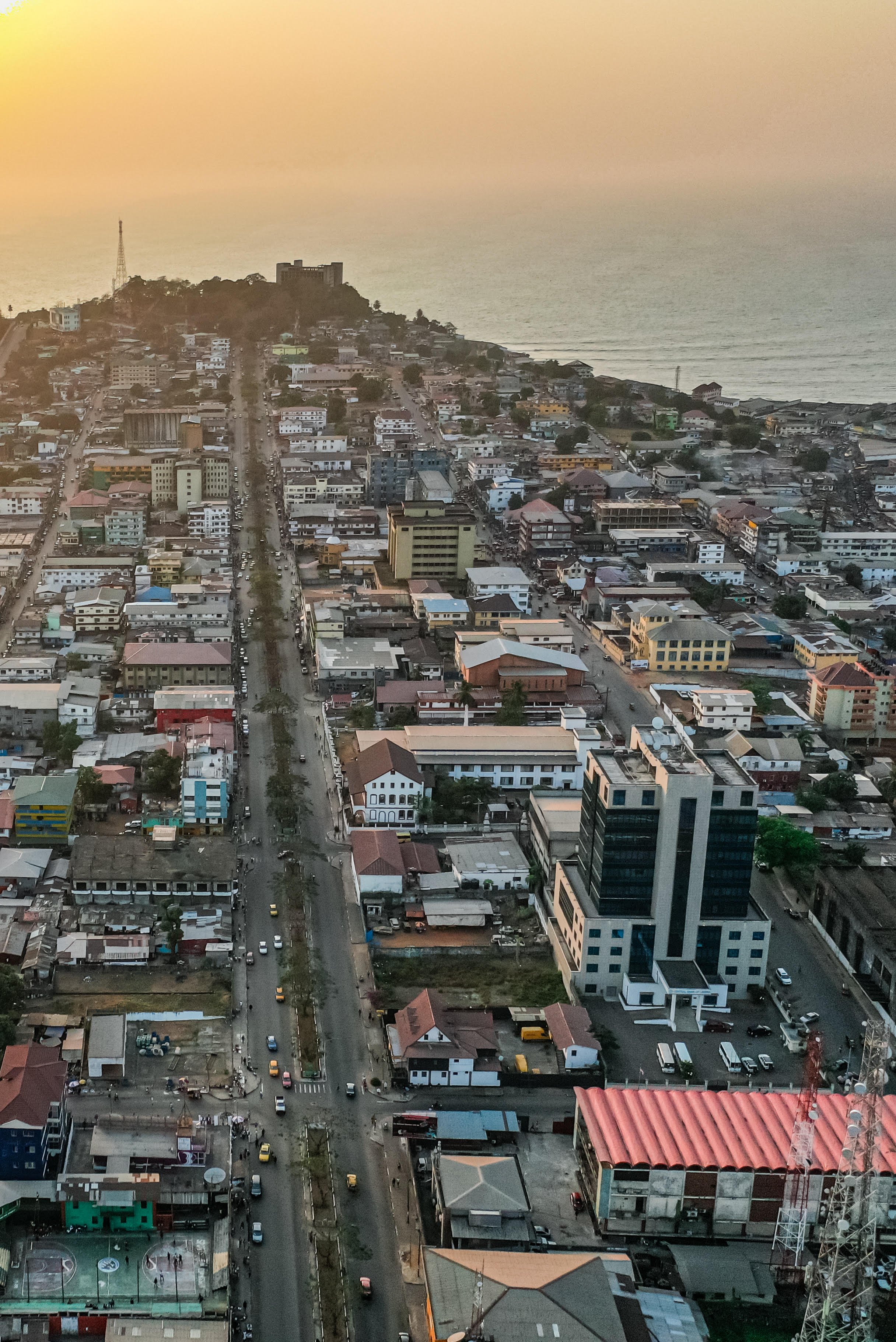 An aerial view of a coastal city during sunset, showing buildings, streets, and the ocean in the background.