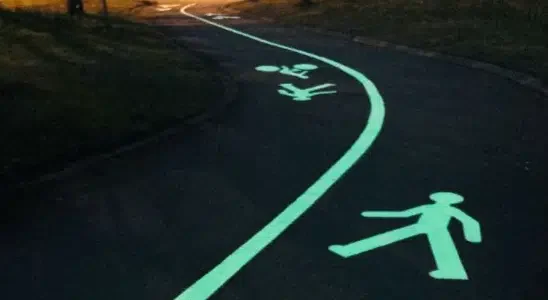Glow-in-the-dark road markings depicting a walking path and pedestrian figures at night.