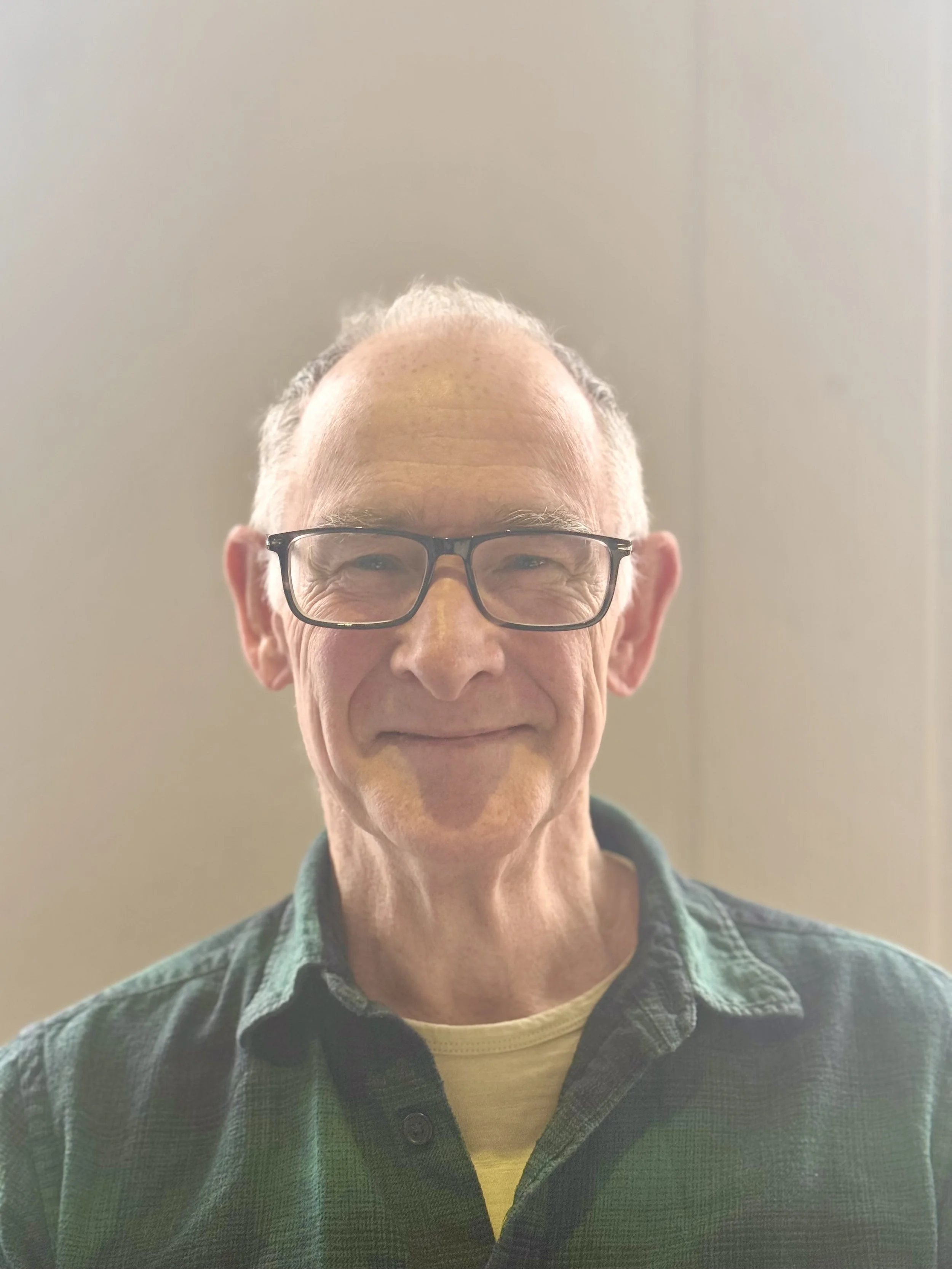 Elderly man with glasses, smiling, wearing a green shirt