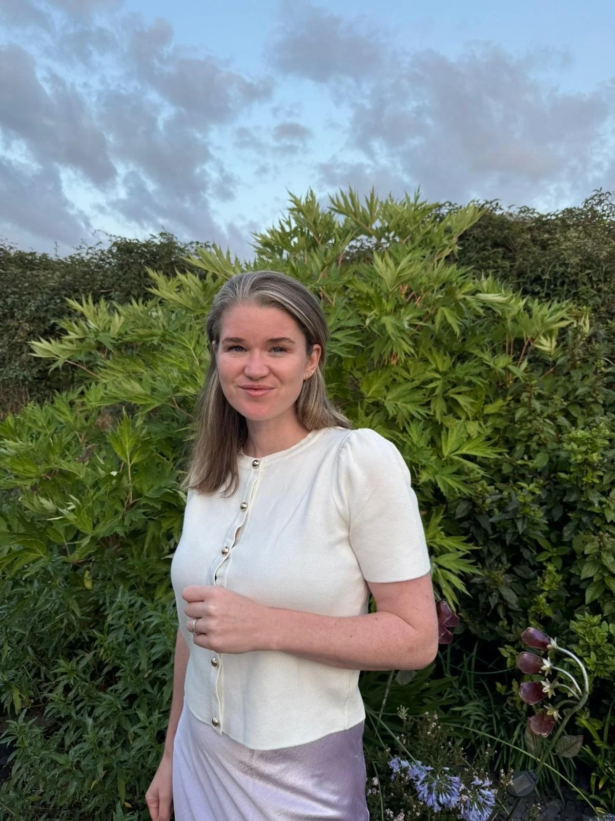 Person wearing glasses and smiling indoors, with a clock on the wall in the background.