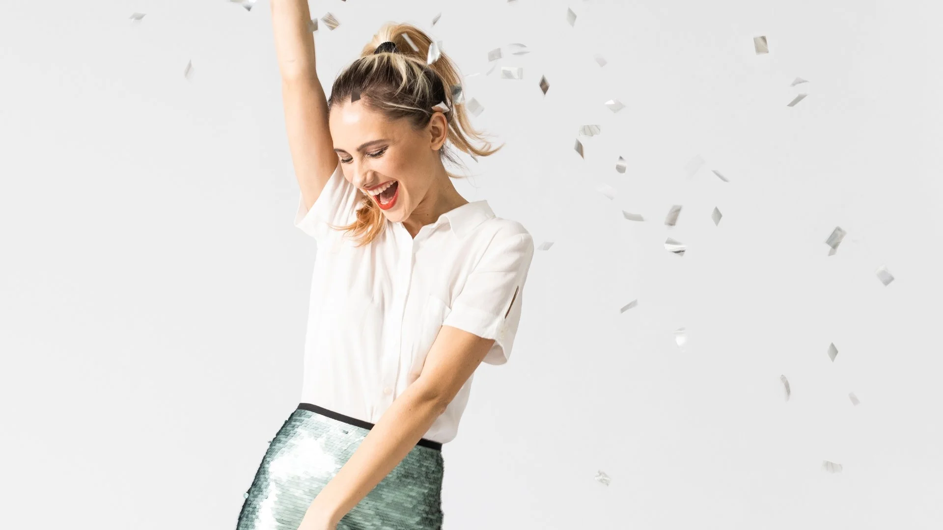 Mujer joven celebrando con confeti en un fondo blanco.