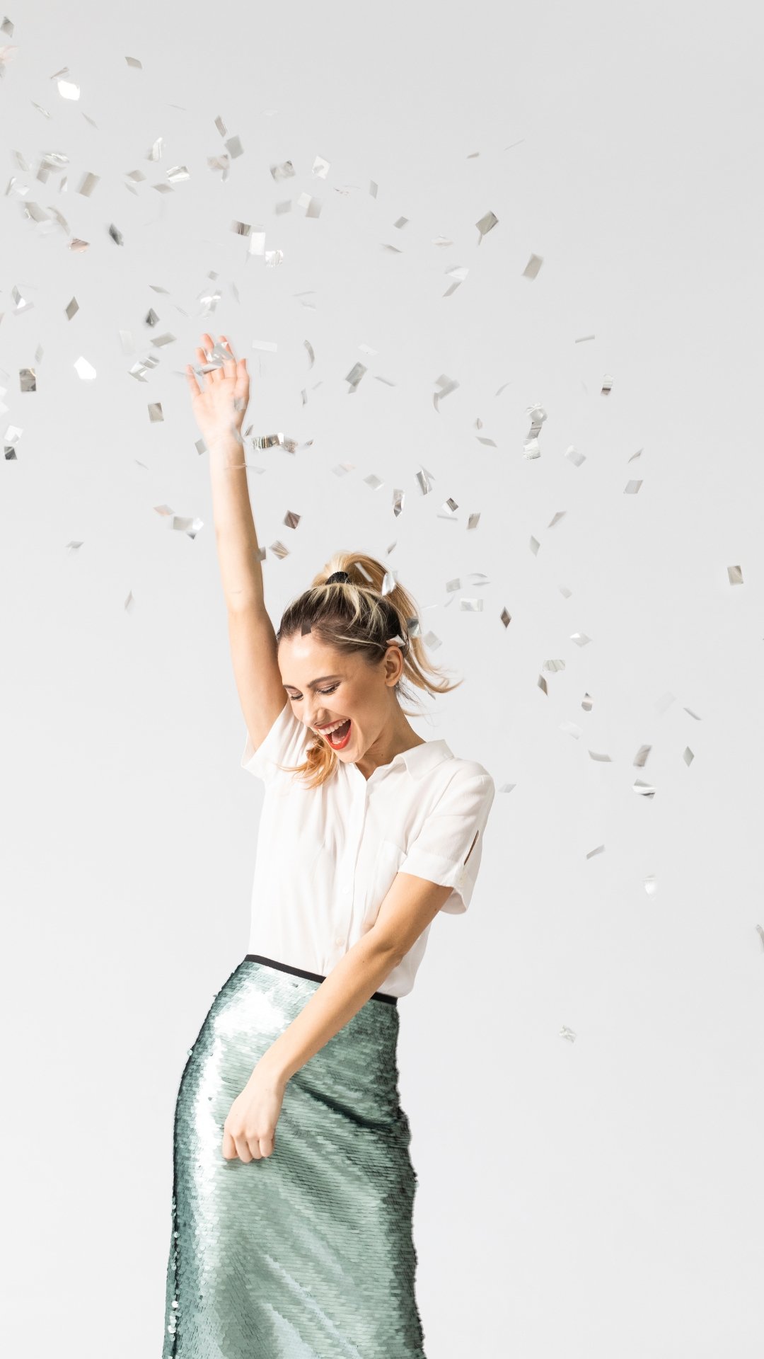 Mujer feliz lanzando confeti plateado en un fondo blanco.