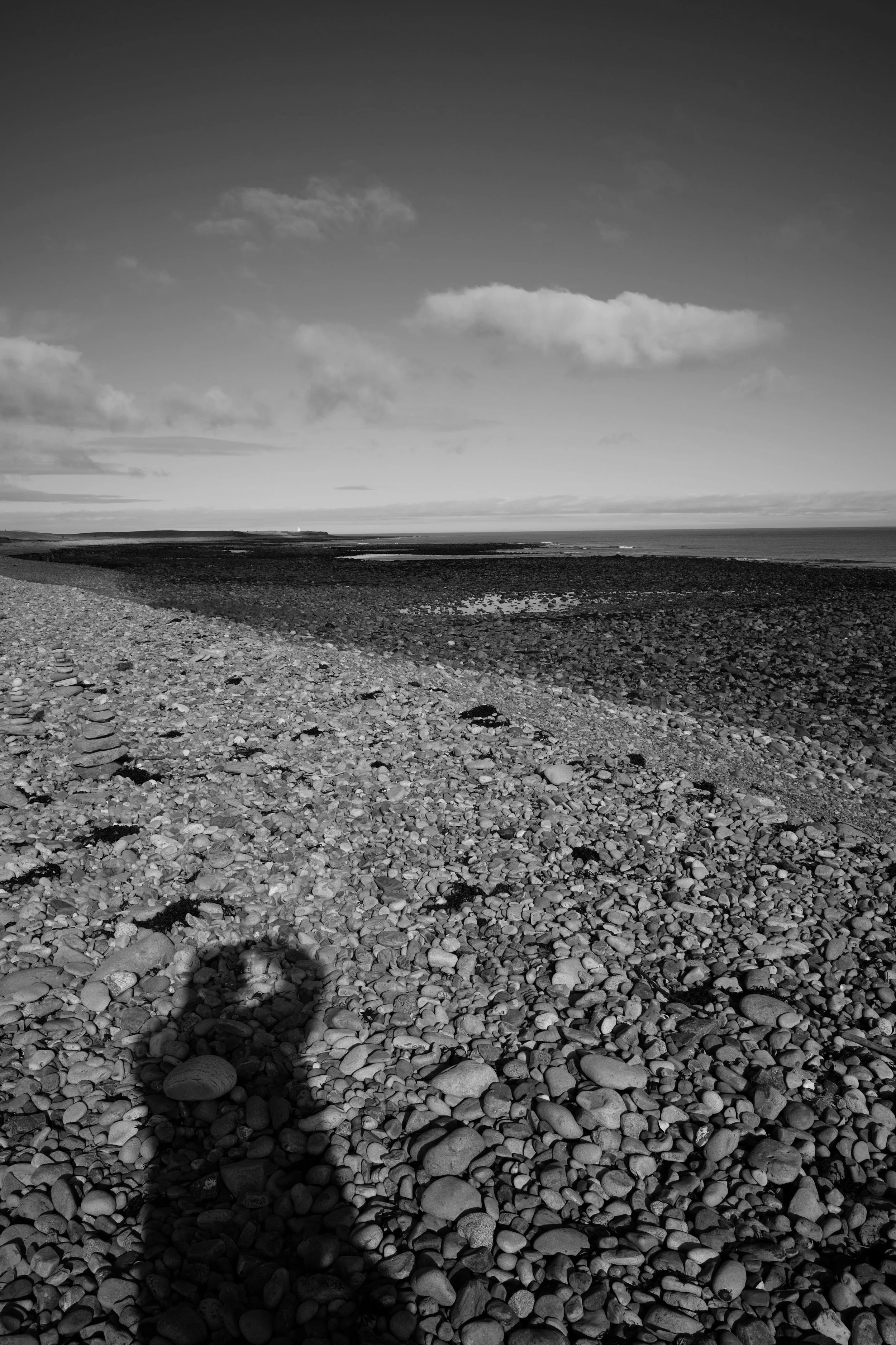A beach, so still and quiet. The crunch of heel on stone, the trodden march of ages. A shadow falls upon the rocks, natures path recorded. 