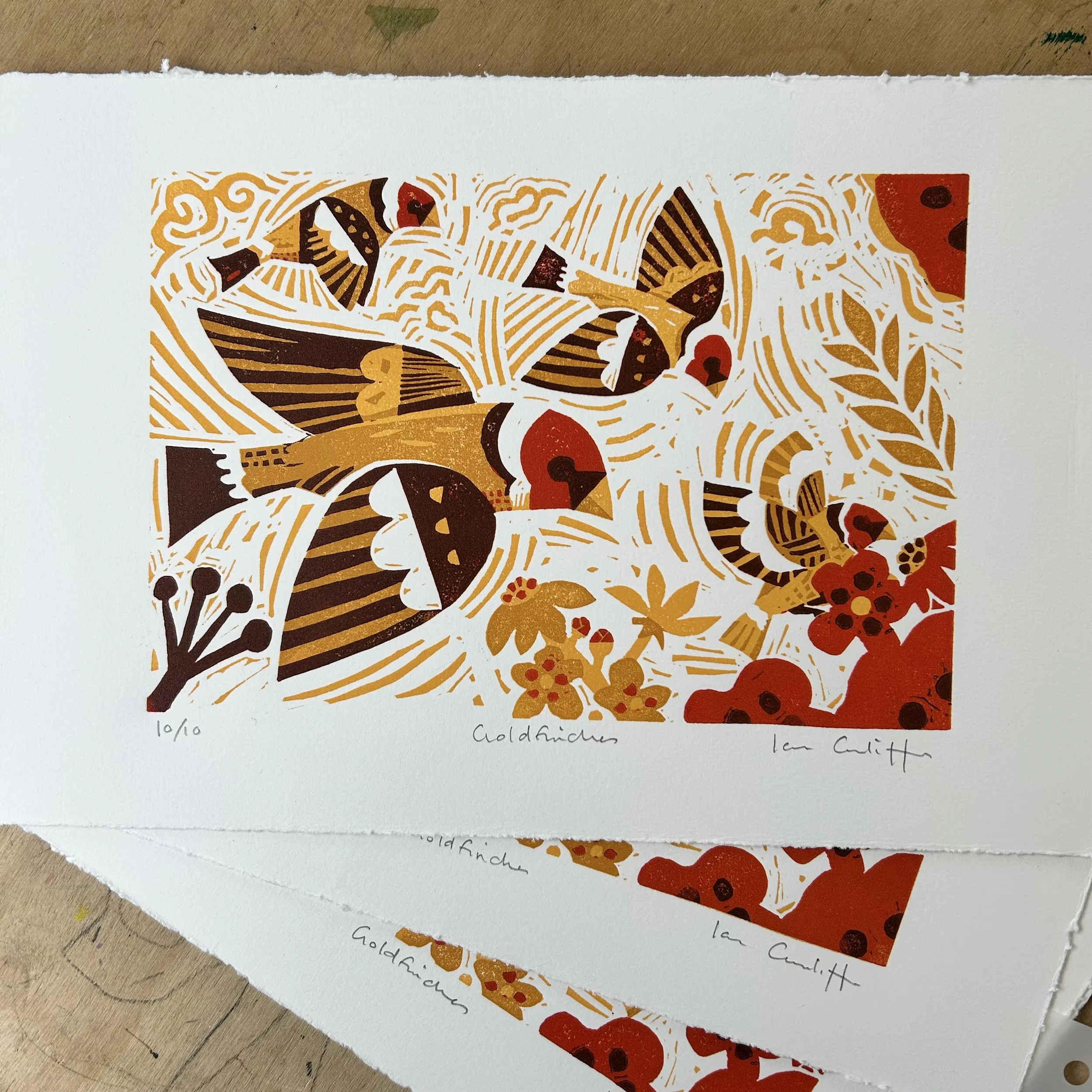 Close-up of a botanical illustration on white paper, featuring butterflies and flowers in shades of gold, black, red, and brown, with handwritten text and numbering at the bottom.