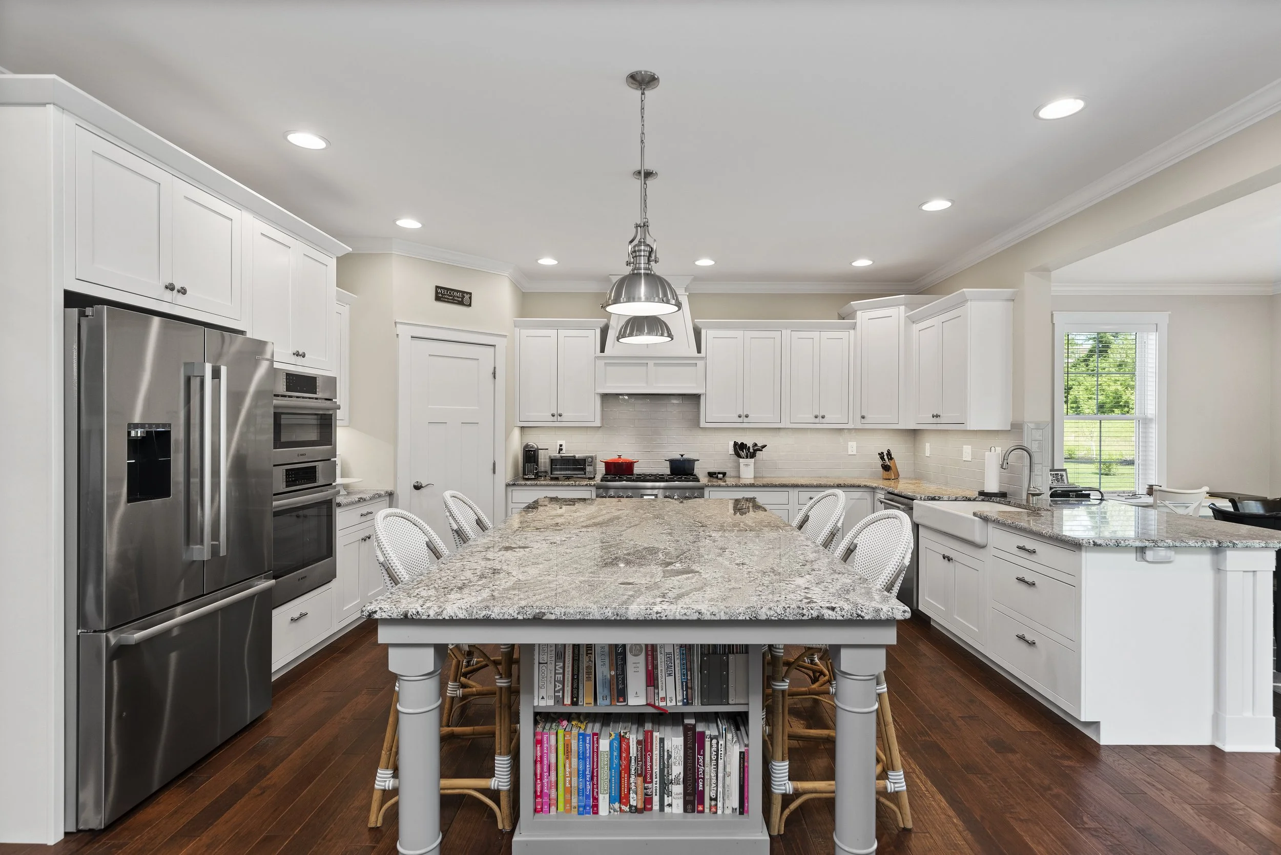 Modern kitchen with white cabinets, granite countertops, stainless steel appliances, and a central island with bookshelves and chairs.