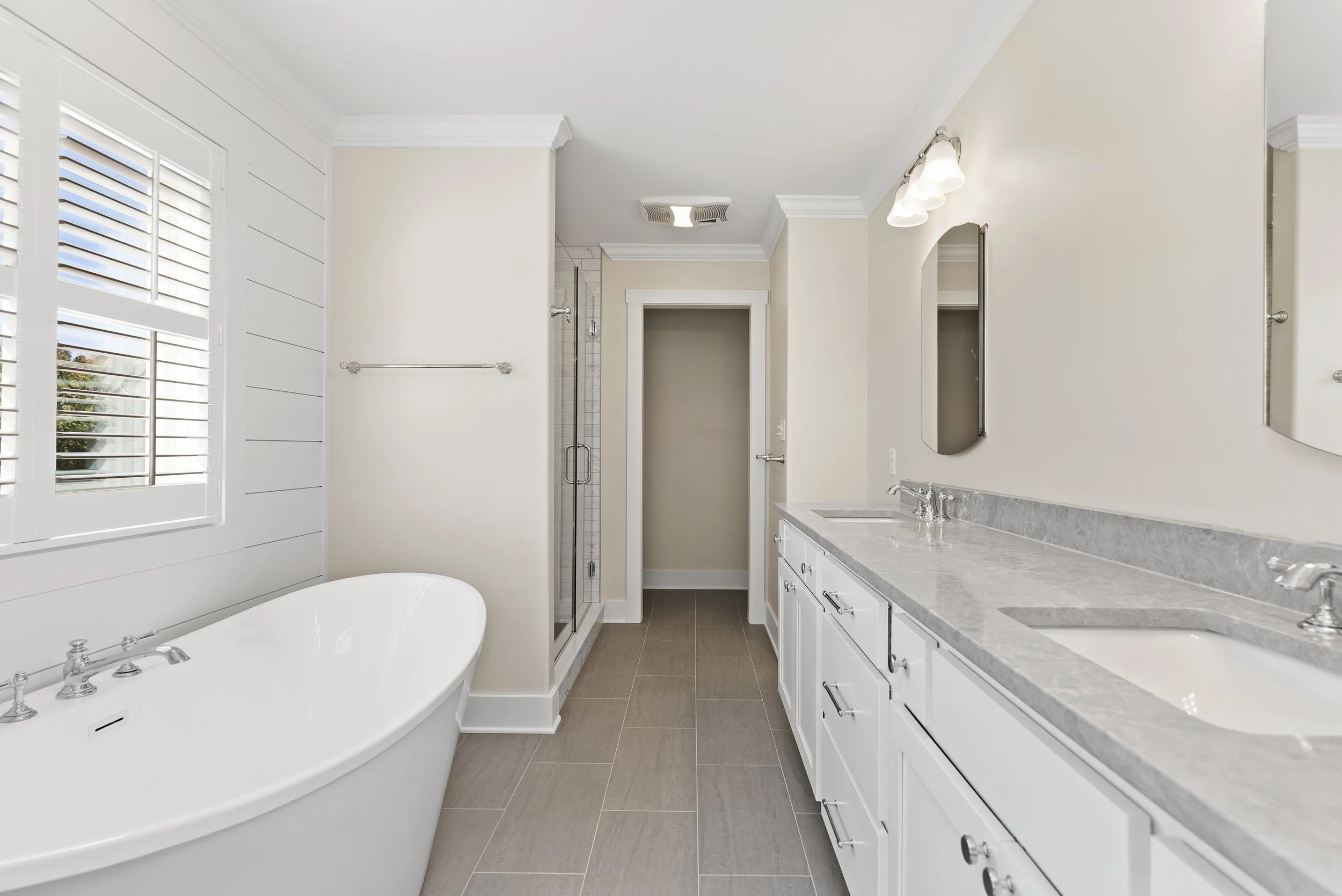 Modern bathroom with freestanding tub, glass shower, white cabinets, and dual sinks.
