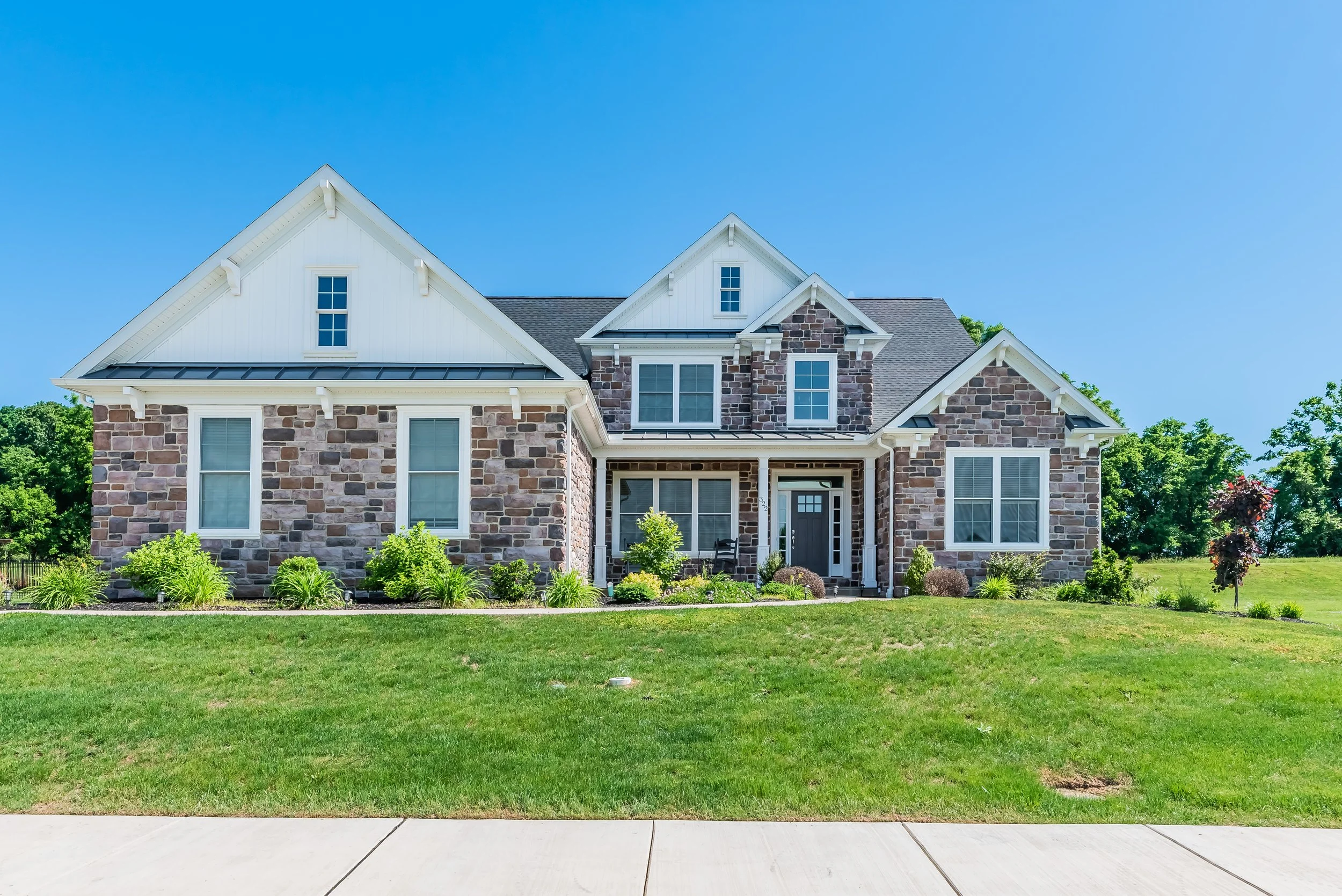 Traditional suburban house with stone facade, landscaped front yard, and a blue sky.