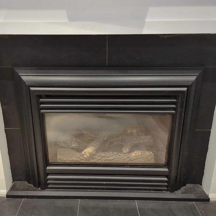 Gas fireplace insert with black tile surround and white mantel, before cleaning