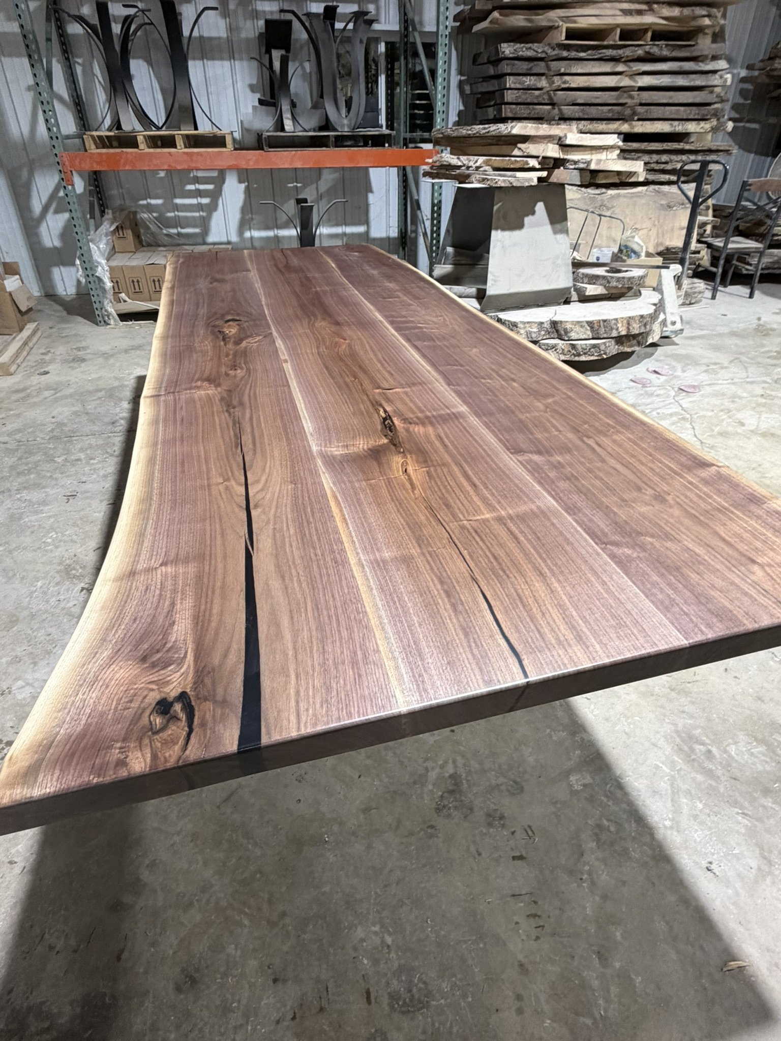 A large, polished wooden slab with natural edges and visible grain patterns, resting on a workbench in a woodworking workshop.