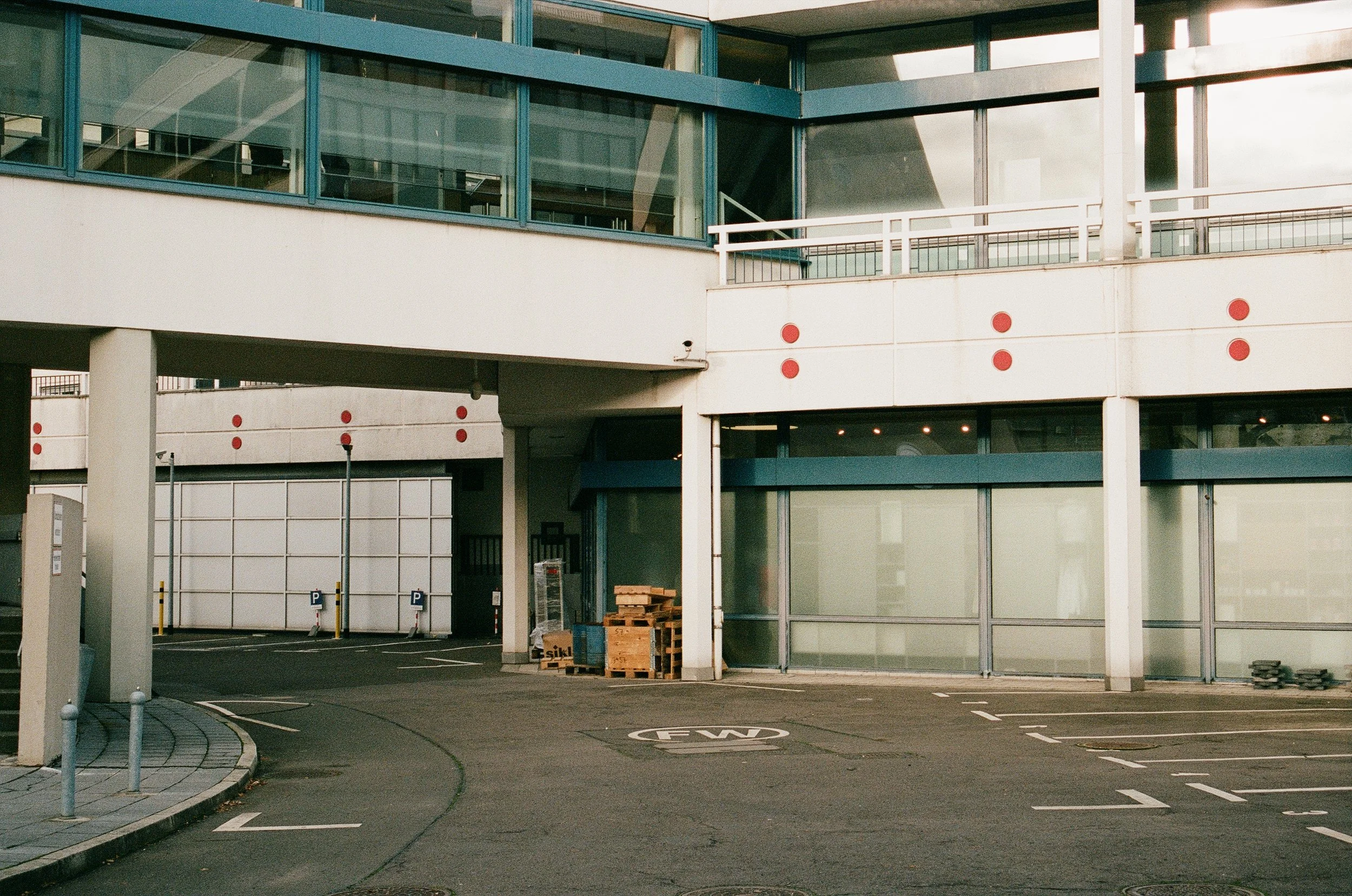 Empty parking lot in front of a modern building with large glass windows and red circular markers on the walls.