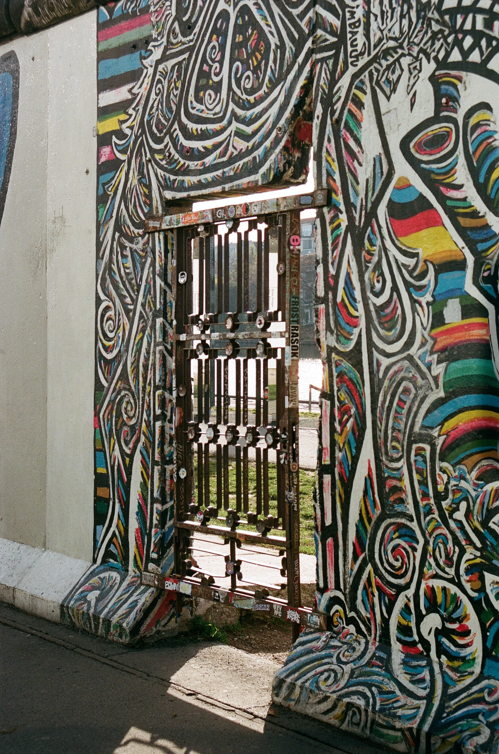 A graffiti-covered wall with a metal gate in the center, leading outside. The graffiti features colorful, swirling abstract designs with black and white outlines.