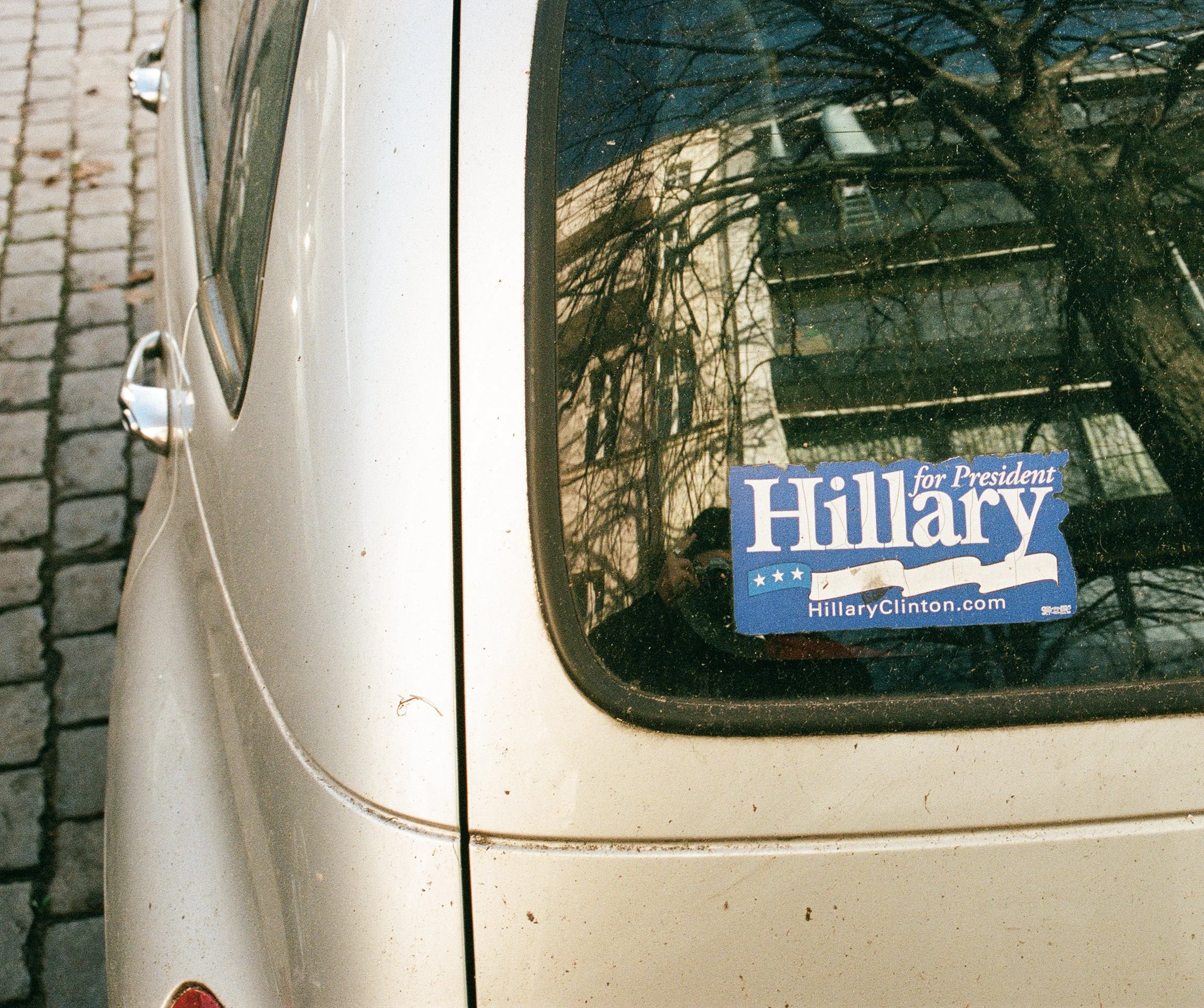A vehicle with a Hillary Clinton 'Hillary for President' campaign sticker on the rear window.