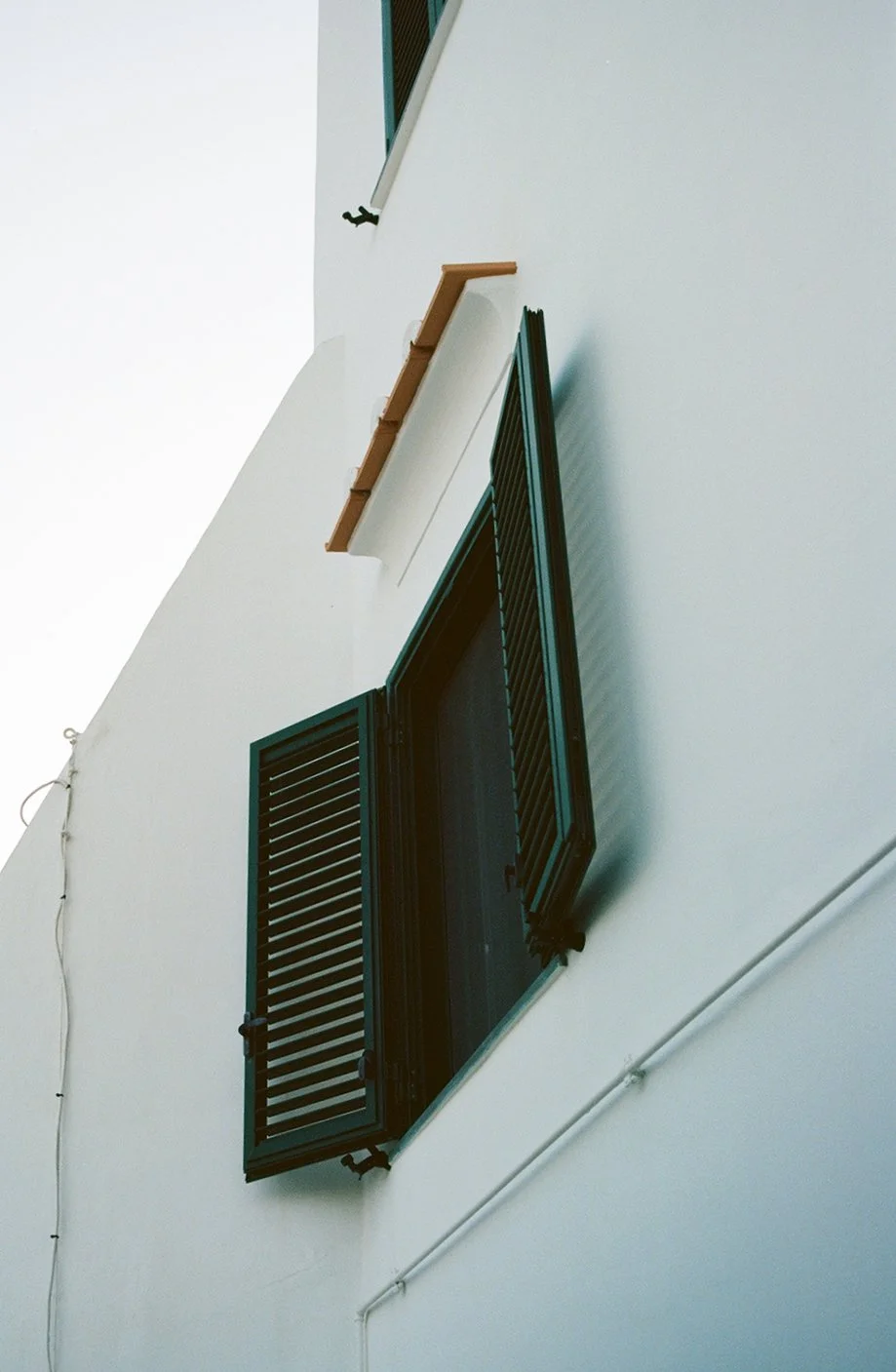 Close-up of a white building facade with an open black window shutter.