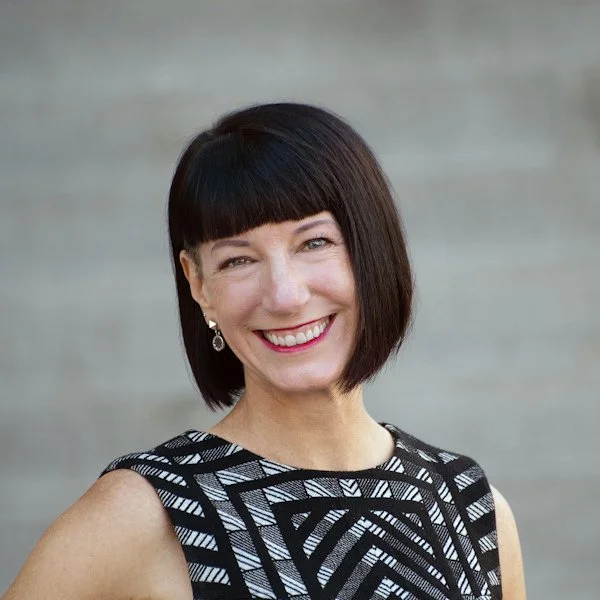 Woman with chin length dark brown hair. Black and white patterned sleeveless top.