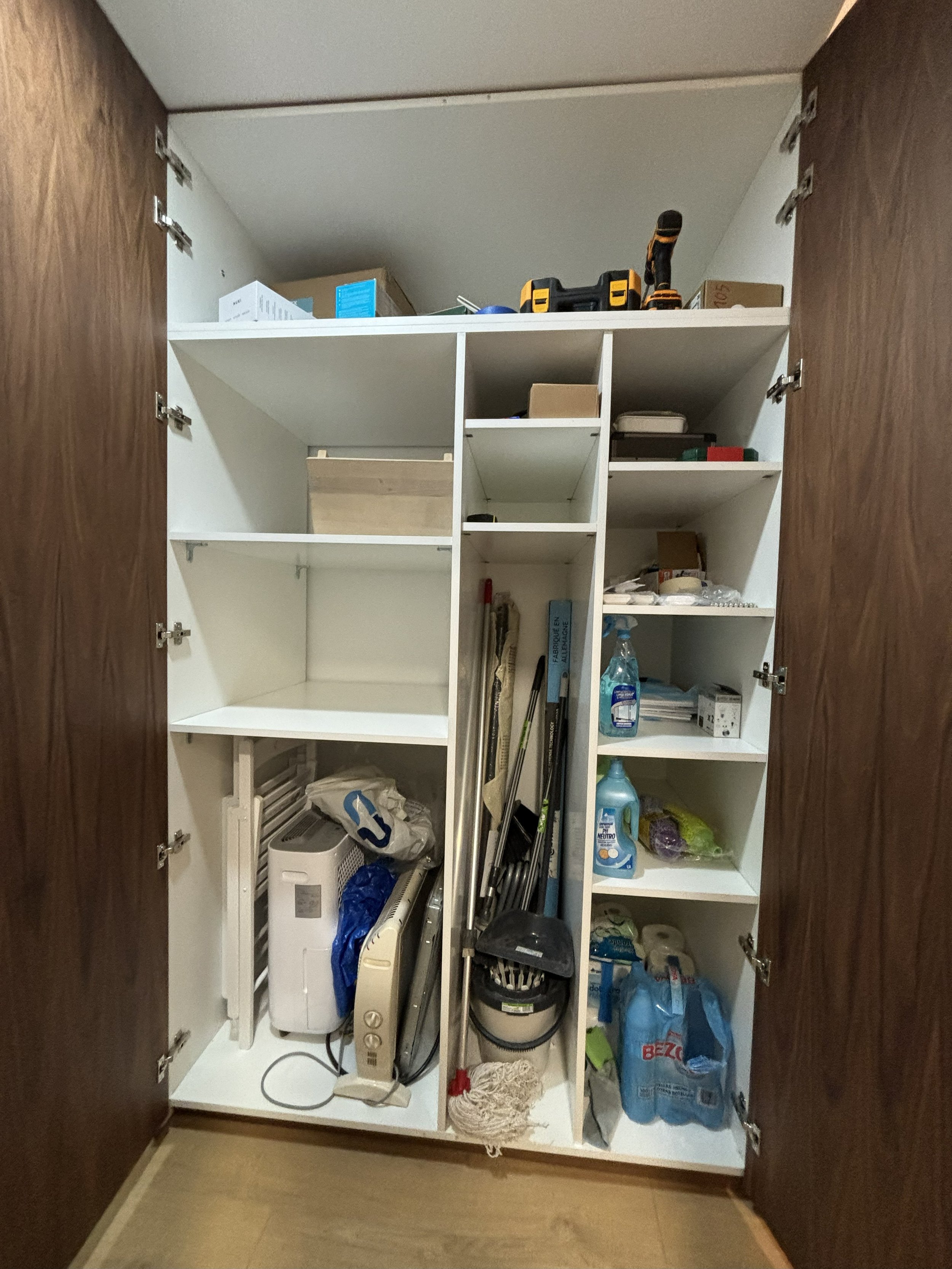 Un armario abierto con diferentes estantes que contienen herramientas, productos de limpieza, y objetos diversos.