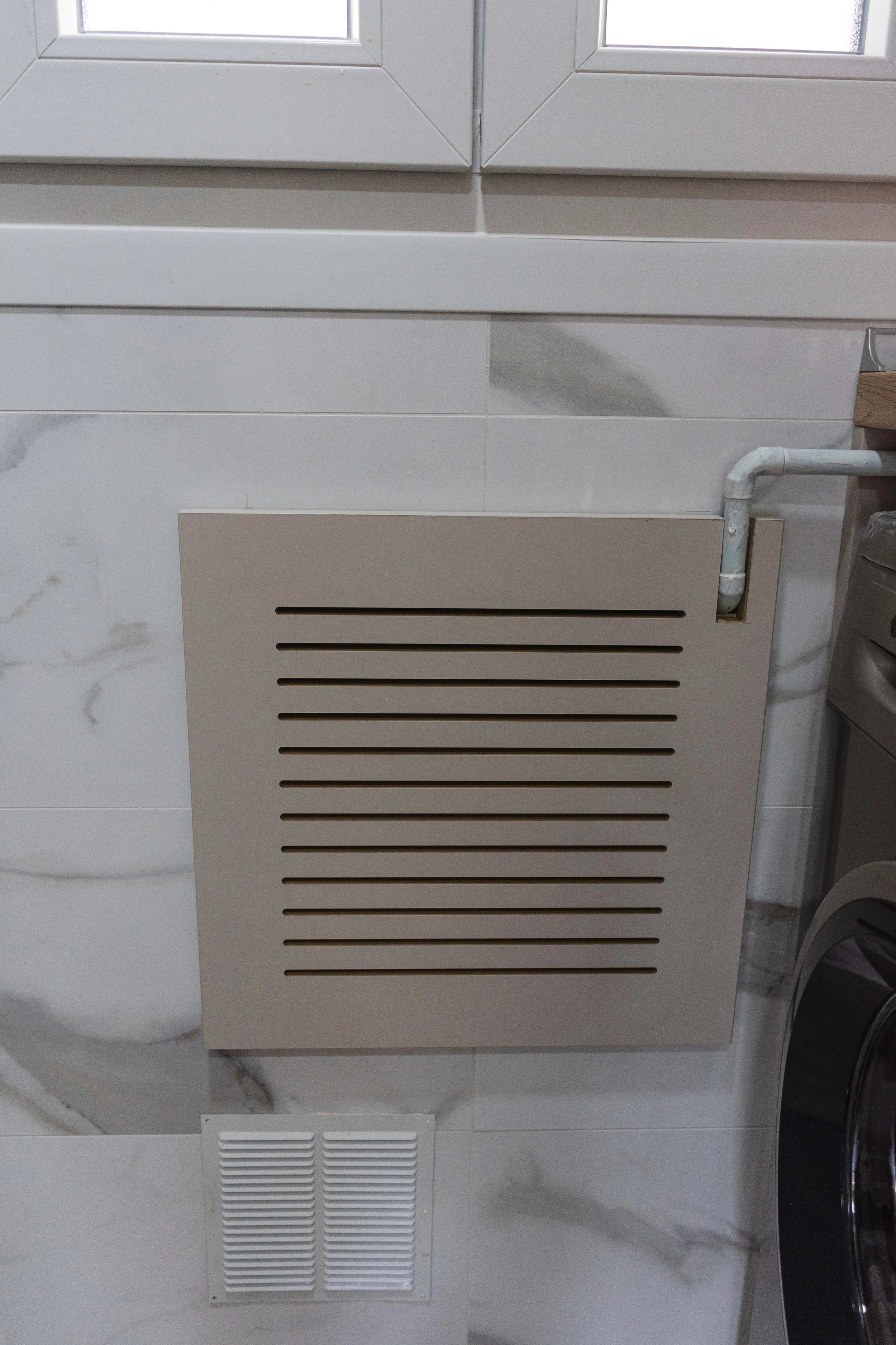 Ventilador de calefacción o aire acondicionado instalado en la pared de una lavandería, con un ventilador de extracción en la parte inferior.