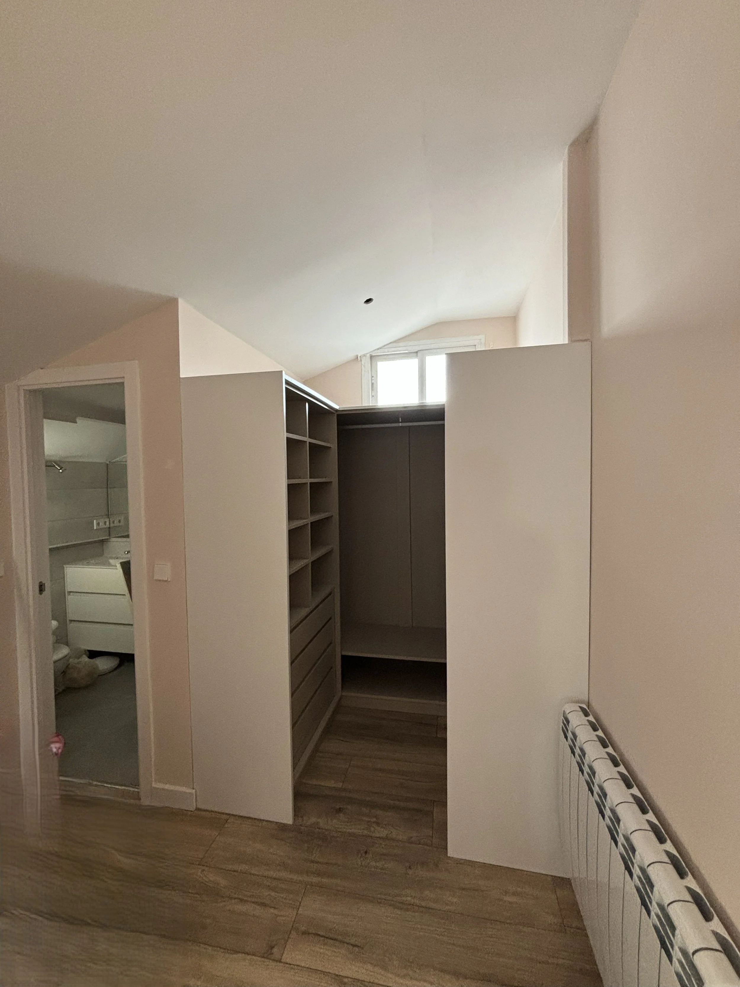 Mueble de armario en una habitación con paredes blancas y suelo de madera, y una ventana en el techo.